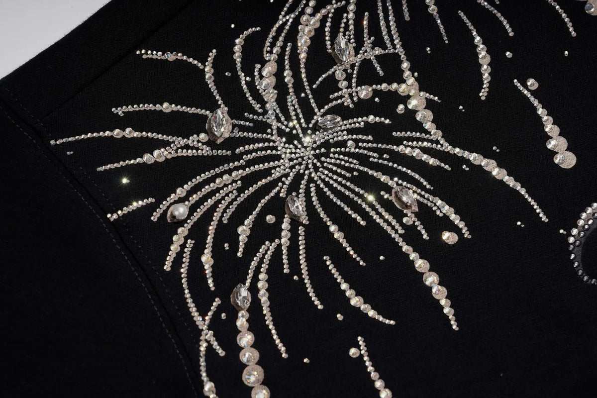 Close-up of a black garment featuring elaborate silver beaded embroidery in a fireworks or burst pattern with pearl-like accents. TCH Rhinestone Firework Graphic Black Sweatshirt