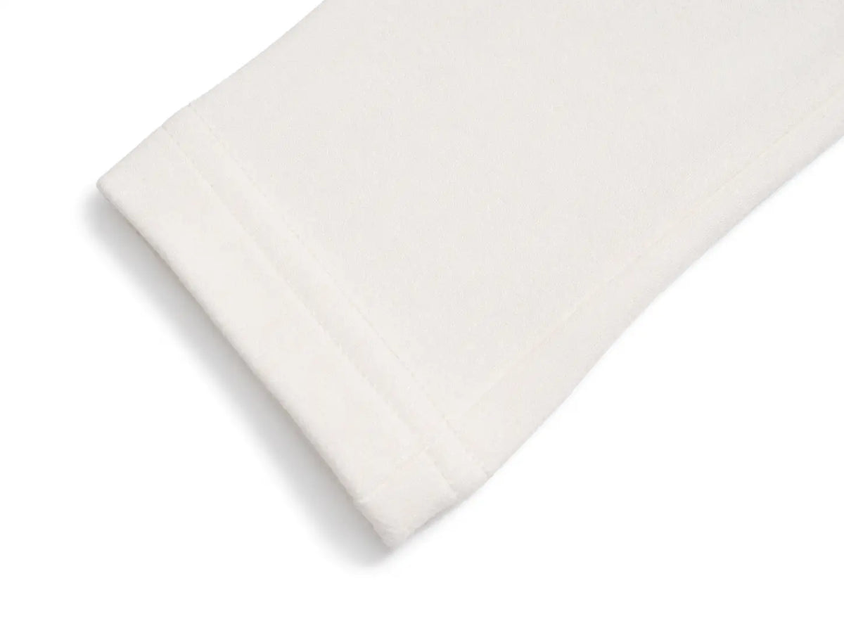 A close-up of a folded off-white or cream-colored fabric, showing its soft texture and neat stitched edge, set against a plain white background. TCH Rhinestone Fleur-de-Lis Fitted Long Sleeve Top