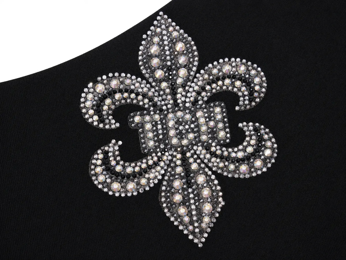 A close-up of a black garment featuring a large, ornate fleur-de-lis embellishment covered in silver rhinestones and white faux pearls. TCH Rhinestone Fleur-de-Lis Fitted Long Sleeve Top