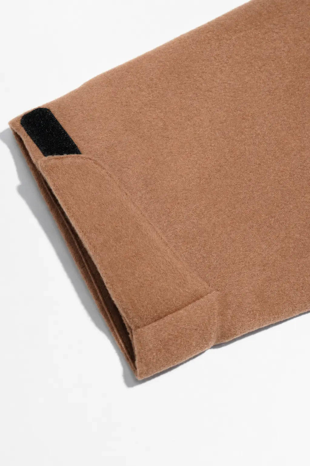A close-up of a folded camel brown wool blanket with a black hook-and-loop closure tab, shot on a clean white background. TCH Rhinestone Fleur-de-Lis Hooded Jacket