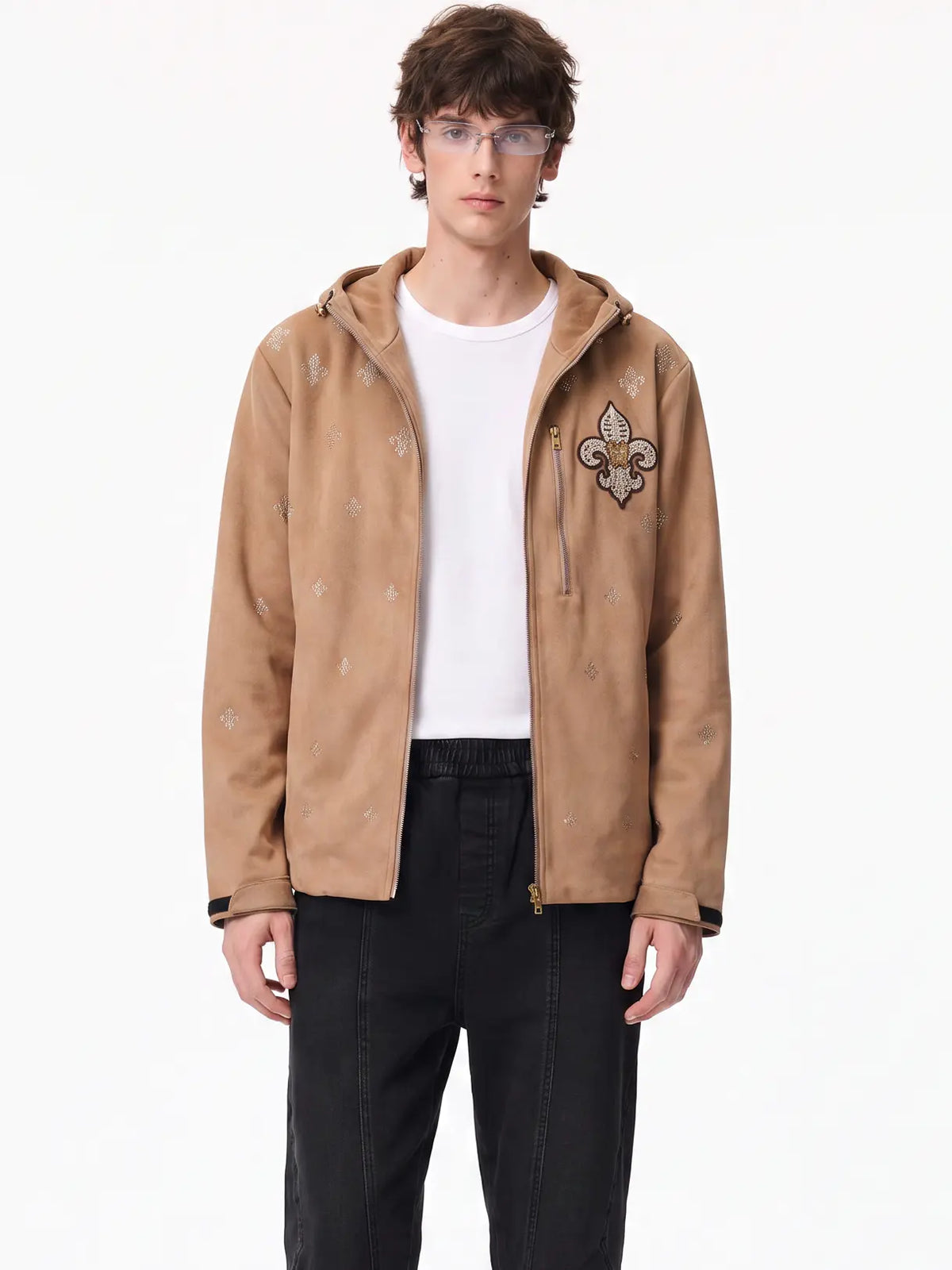 A model wearing a tan hooded zip-up jacket with embroidered fleur-de-lis motifs, layered over a white t-shirt and black pants, against a plain white background. TCH Rhinestone Fleur-de-Lis Hooded Jacket