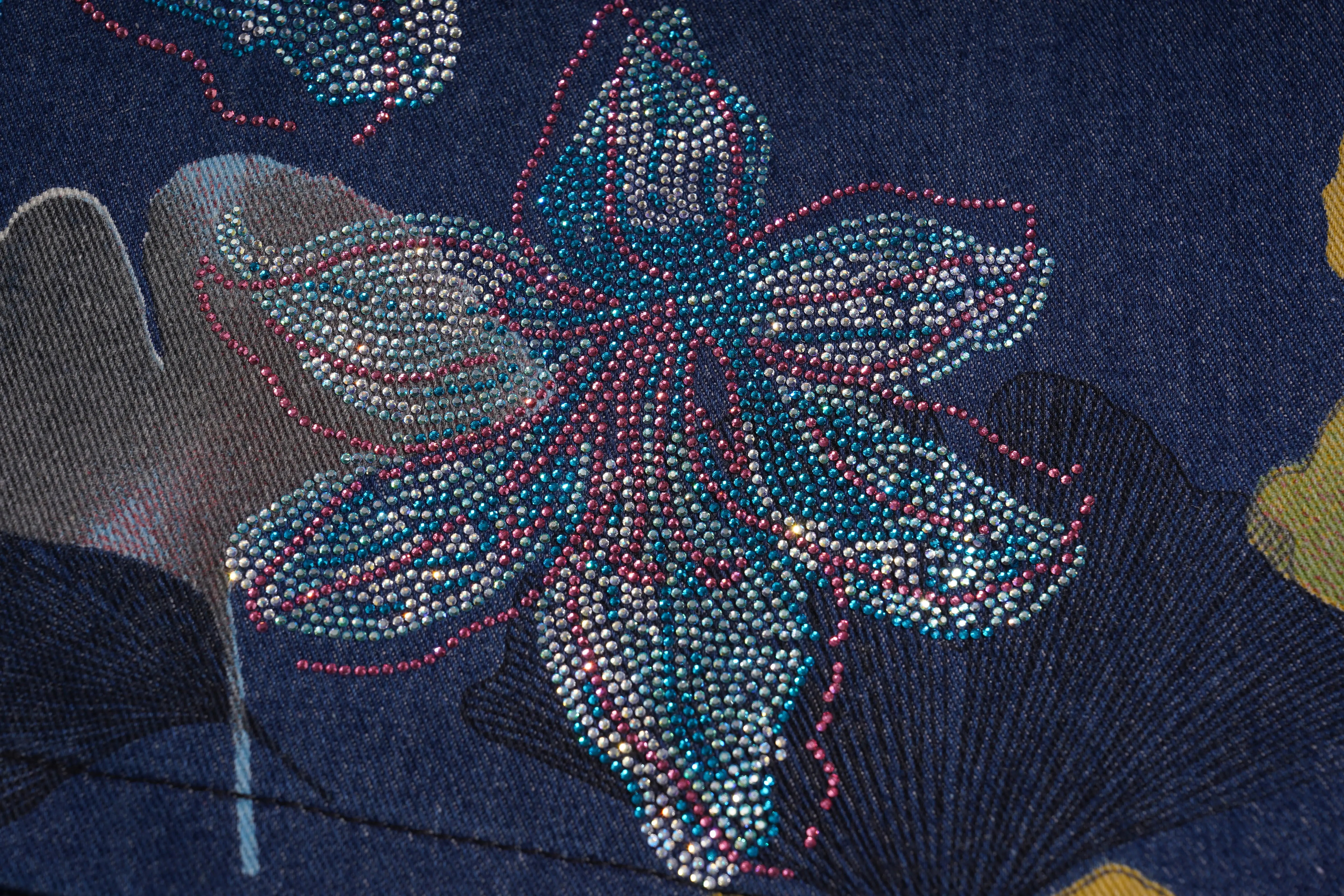 Close-up of a floral embroidery design on fabric with blue and pink colors. TCH Rhinestone Floral Ginkgo Print Denim Shorts