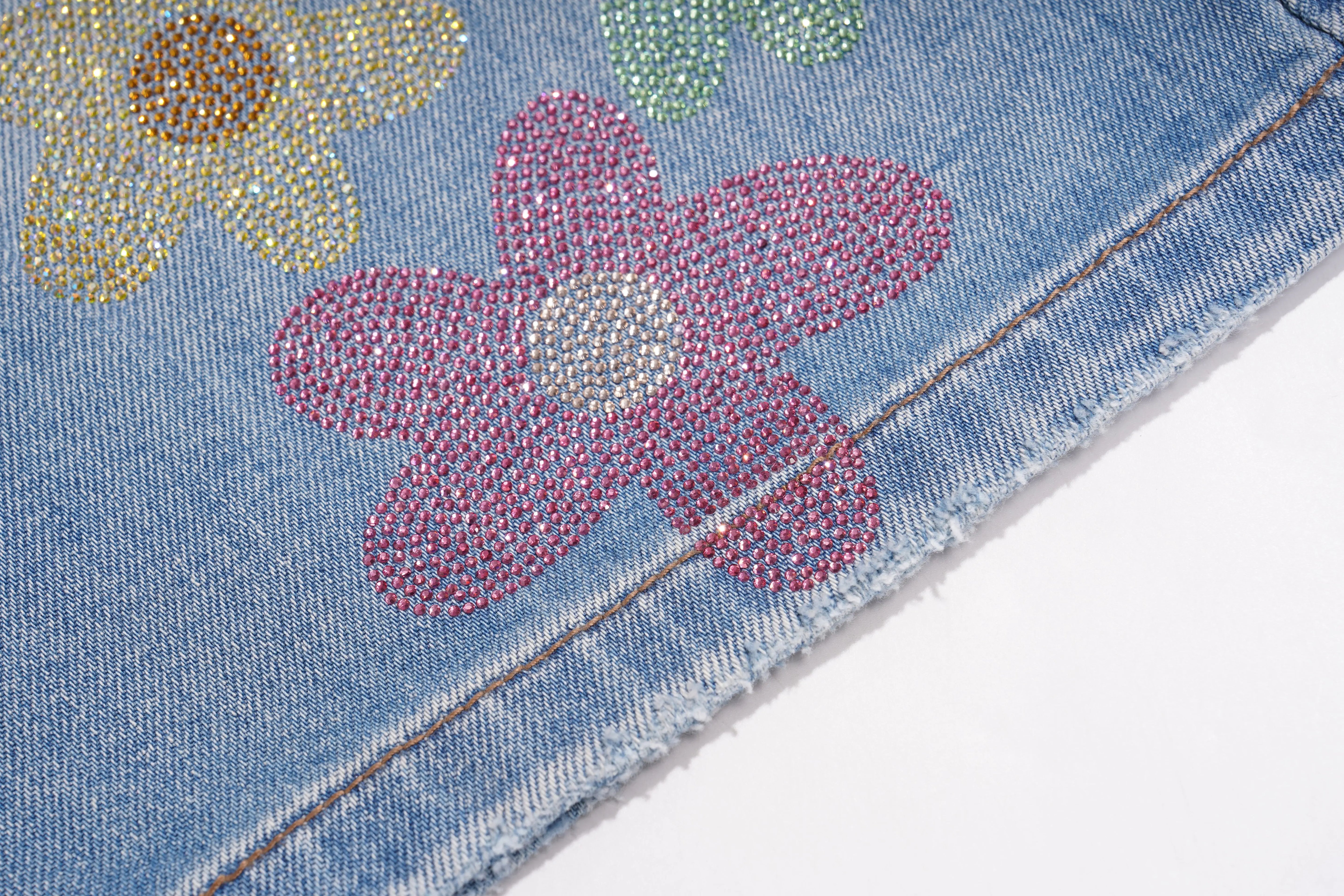 Close-up of denim fabric with floral embellishments on a white background, TCH Rhinestone Floral Logo Wide-Leg Denim Shorts