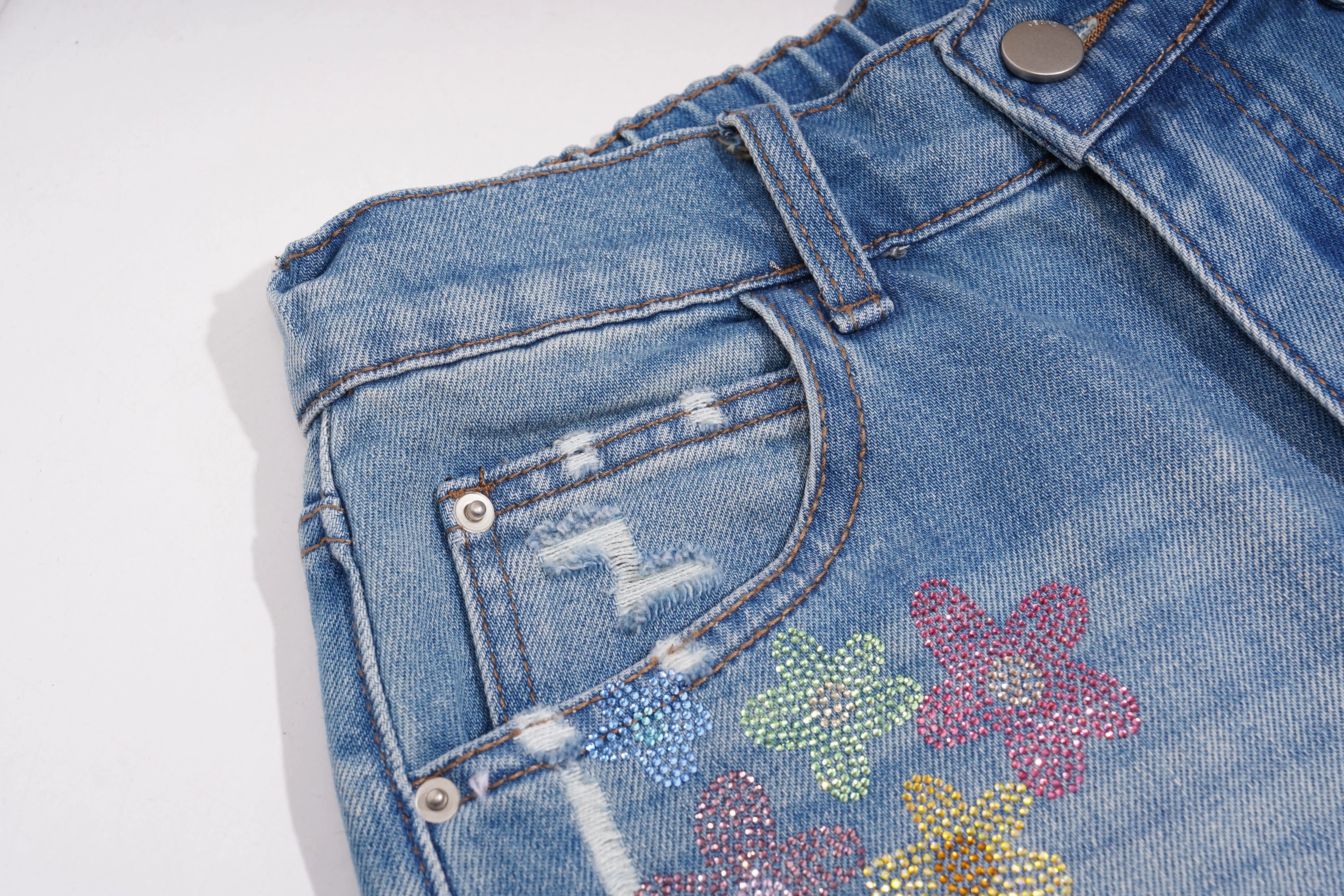 Close-up of blue denim shorts with floral embellishments on a white background, TCH Rhinestone Floral Logo Wide-Leg Denim Shorts
