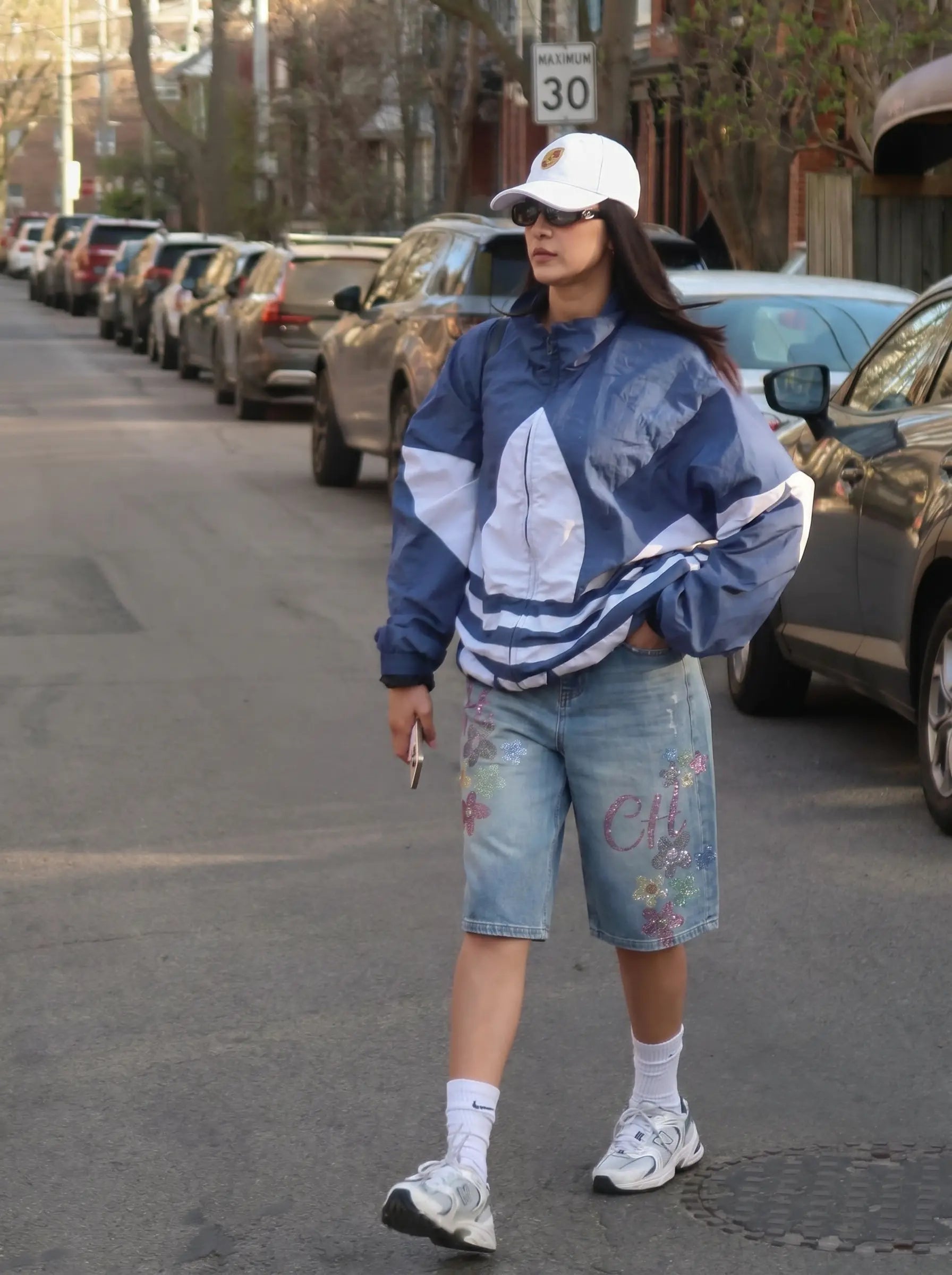 Person walking on a street wearing a blue jacket and denim shorts. TCH Rhinestone Floral Logo Wide-Leg Denim Shorts