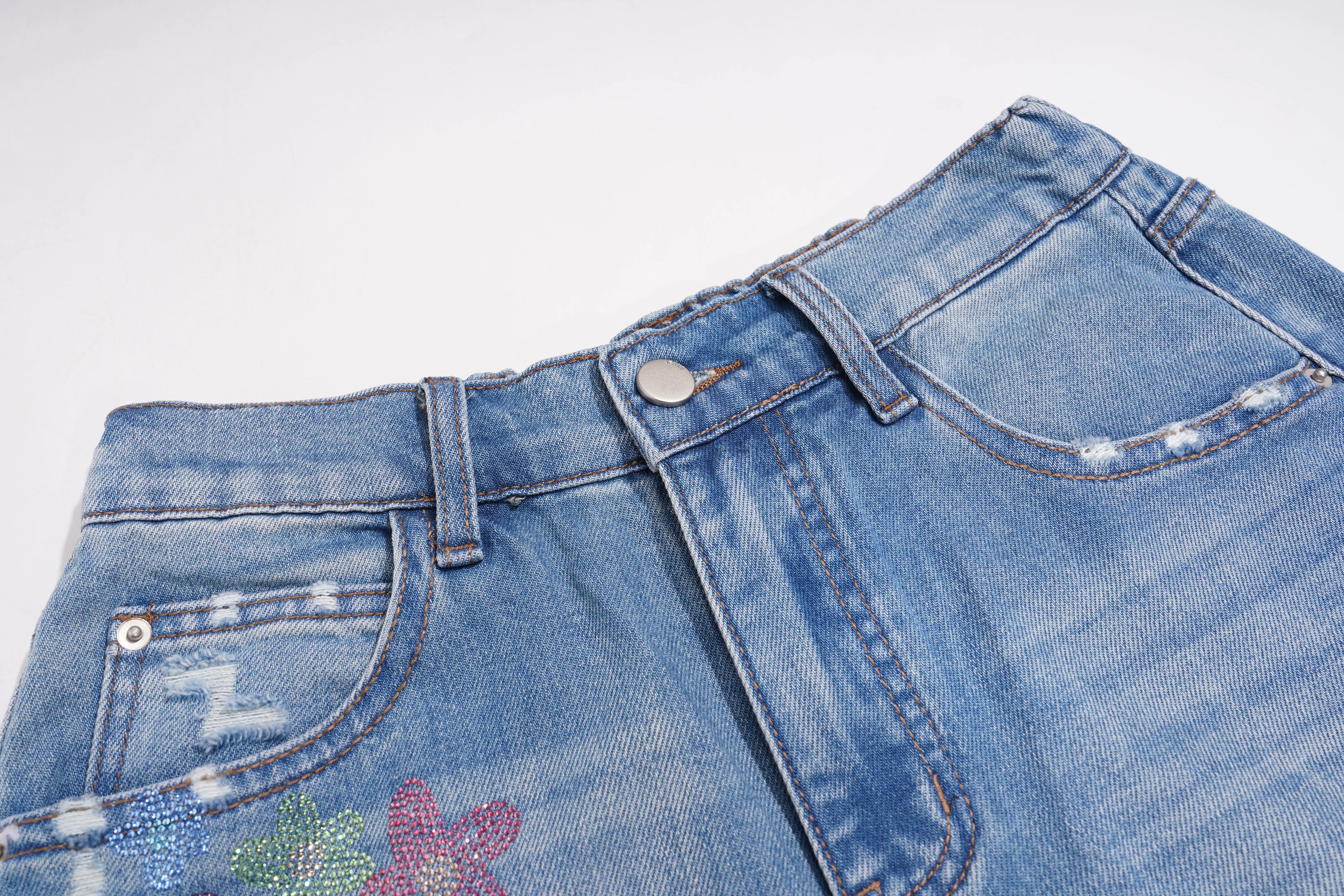 Close-up of blue jeans with floral embroidery on a white background, TCH Rhinestone Floral Logo Wide-Leg Denim Shorts