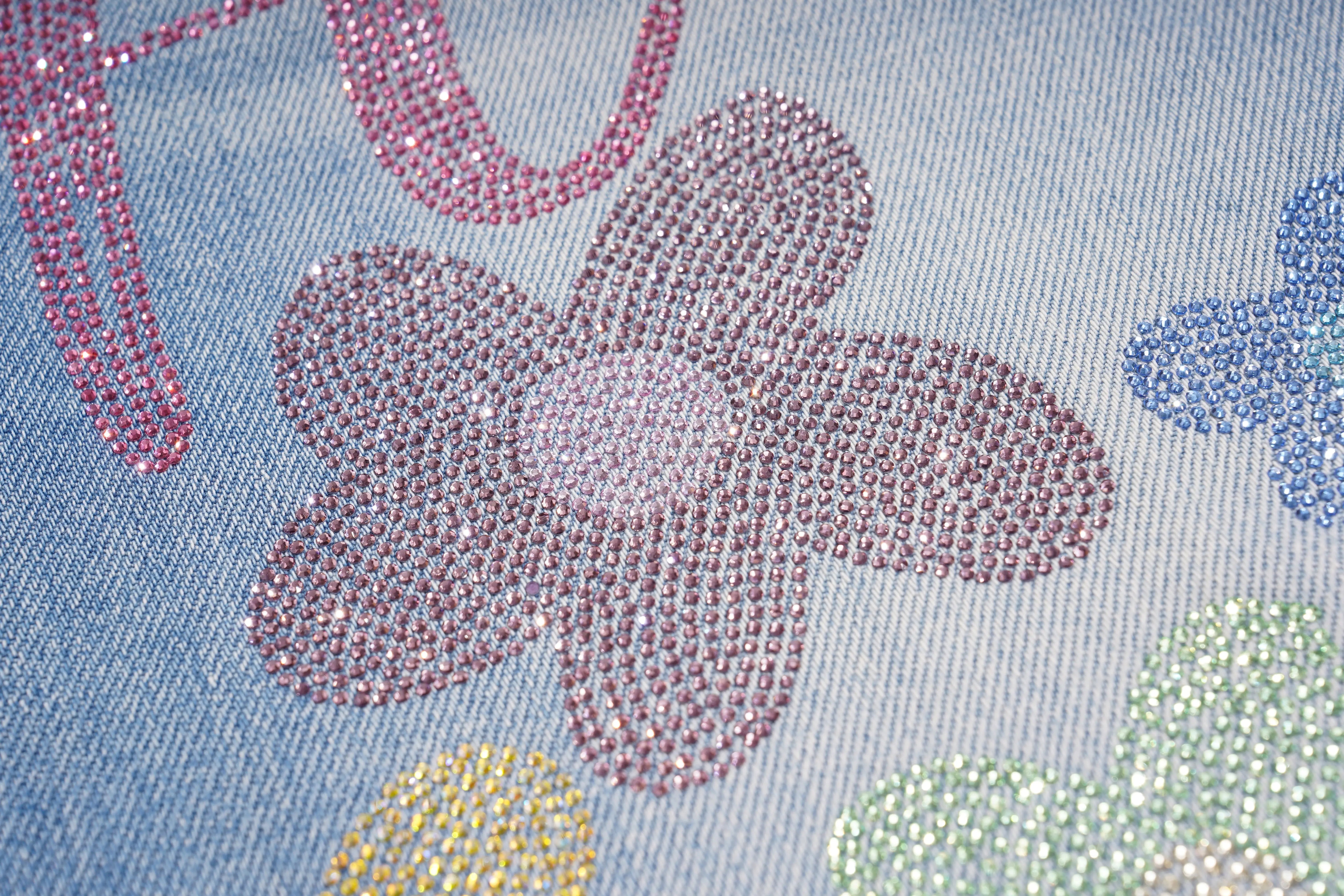 Close-up of denim fabric with colorful rhinestone flowers. TCH Rhinestone Floral Logo Wide-Leg Denim Shorts