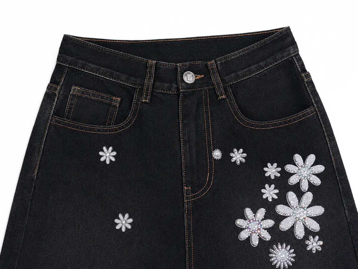 Close-up of a black denim skirt featuring decorative silver rhinestone flower appliqués on the front, shown against a plain white background. TCH Rhinestone Floral Wide-Leg Jeans