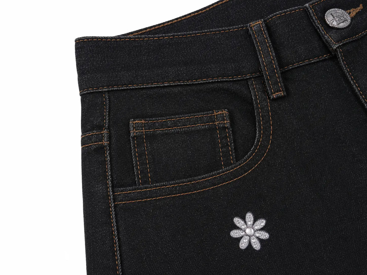 Close-up of black denim jeans showing the back pocket, contrast stitching, a silver button, and a small silver flower embellishment on the leg. TCH Rhinestone Floral Wide-Leg Jeans