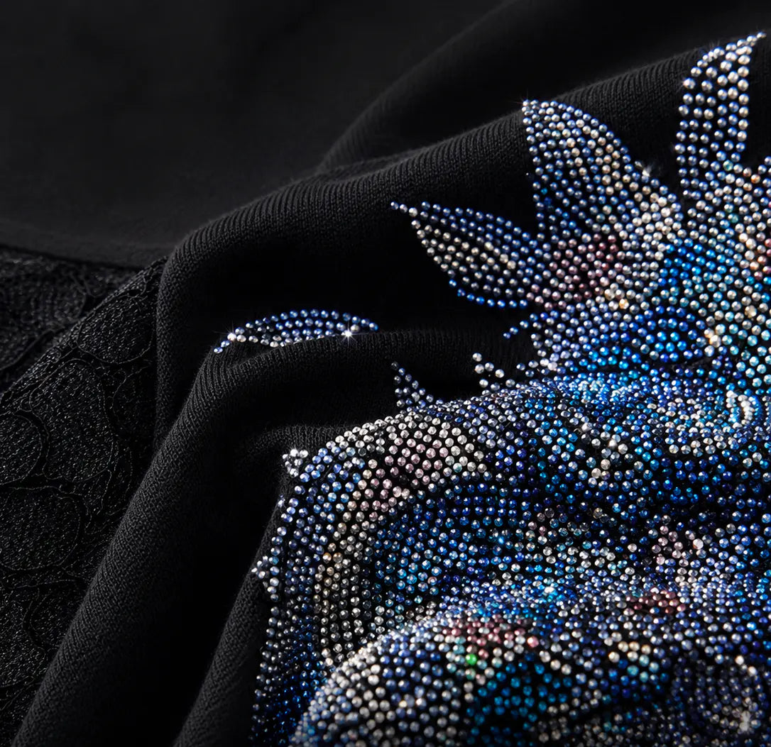 Close-up of a black fabric garment with a large floral embellishment made of blue, silver, and iridescent rhinestones. TCH Rhinestone Floral Wing Techno Graphic T-Shirt