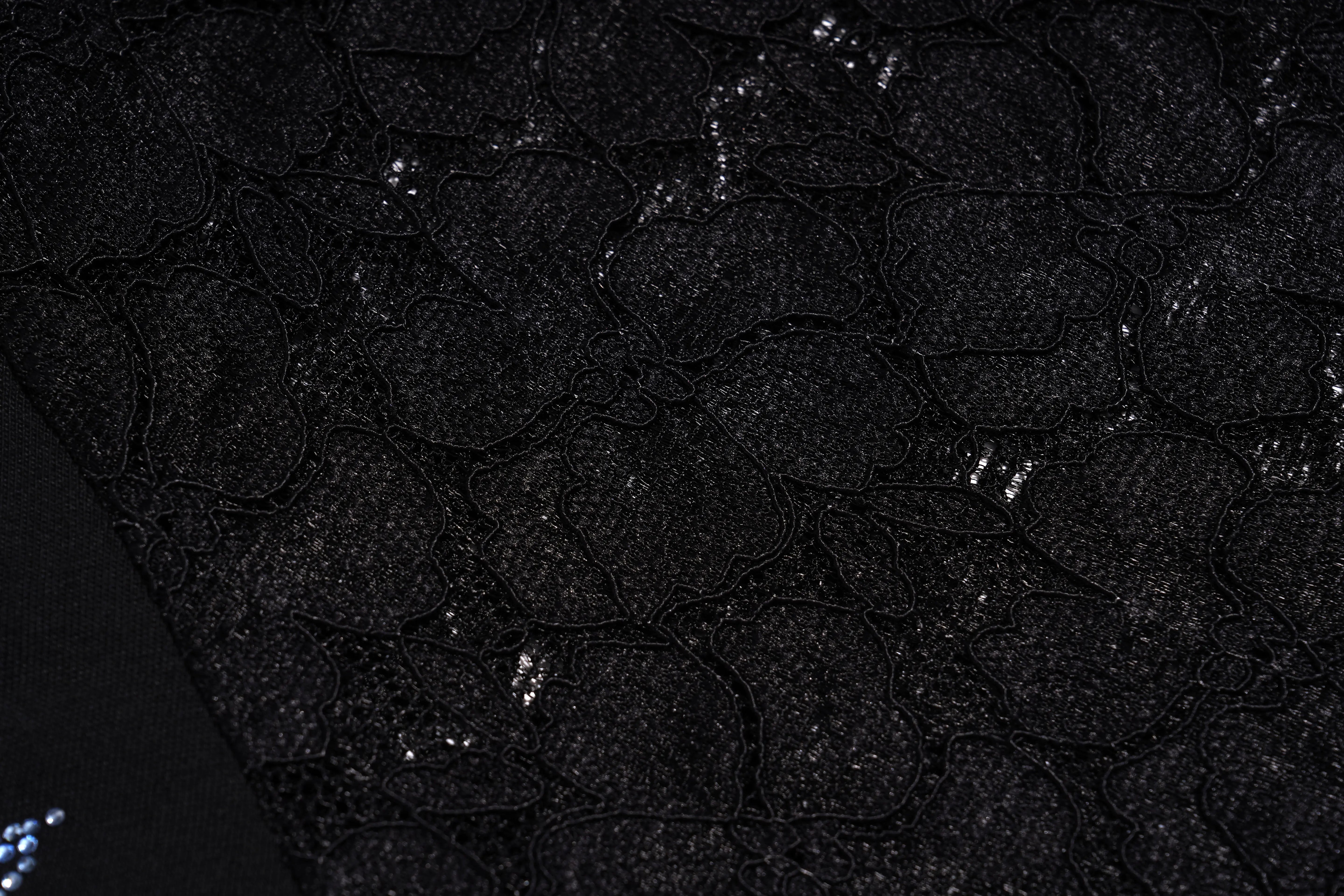 Close-up of a black lace fabric with a textured, scalloped pattern and subtle shimmering sequins. TCH Rhinestone Floral Wing Techno Graphic T-Shirt