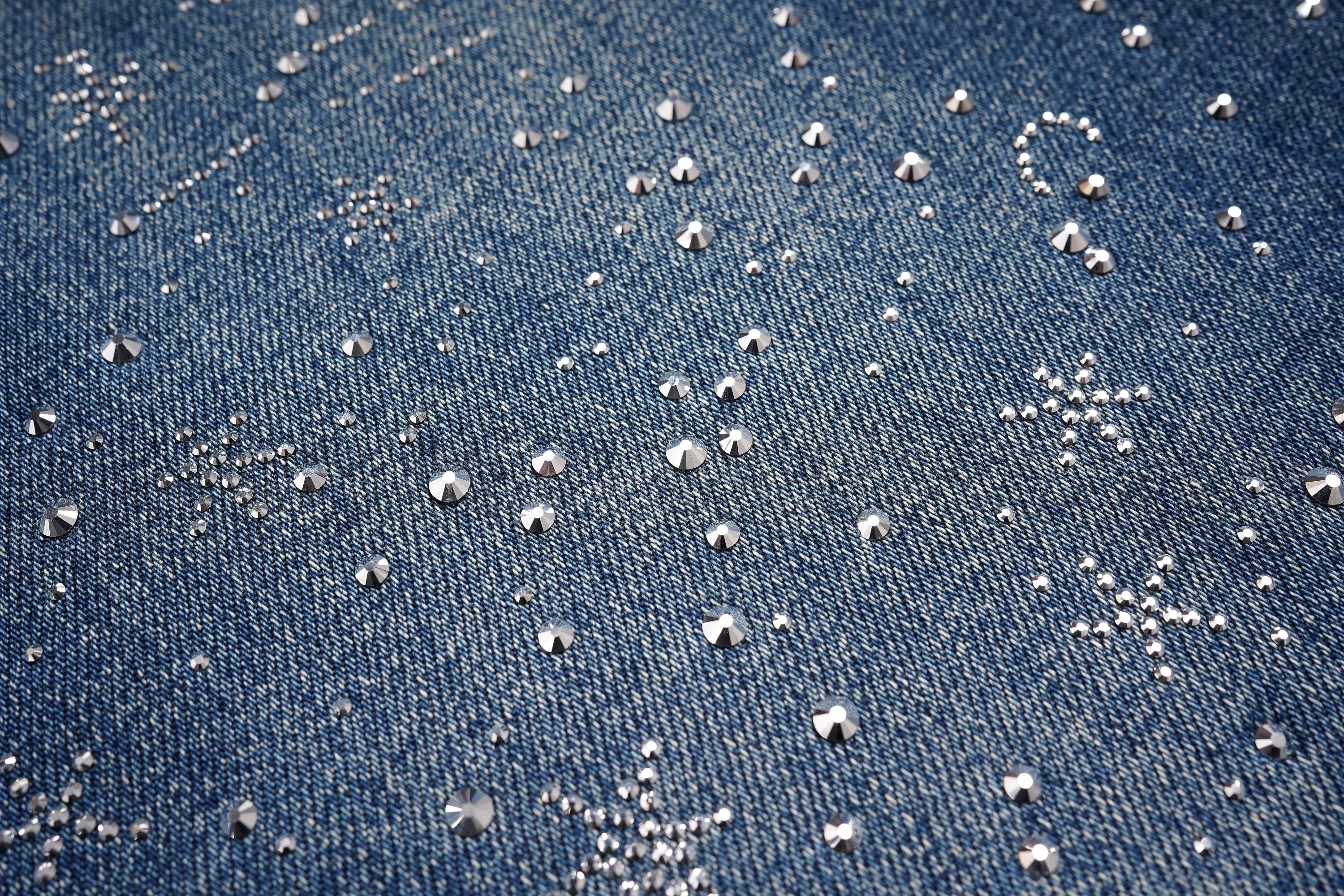 Close-up of blue denim fabric with silver rhinestone embellishments. TCH Rhinestone Galaxy Sparkle Wide-Leg Jeans