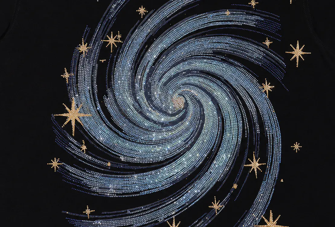 A close-up of a black garment featuring a large spiral galaxy design made of silver rhinestones, accented with gold rhinestone stars. TCH Rhinestone Galaxy Spiral Graphic Black T-Shirt