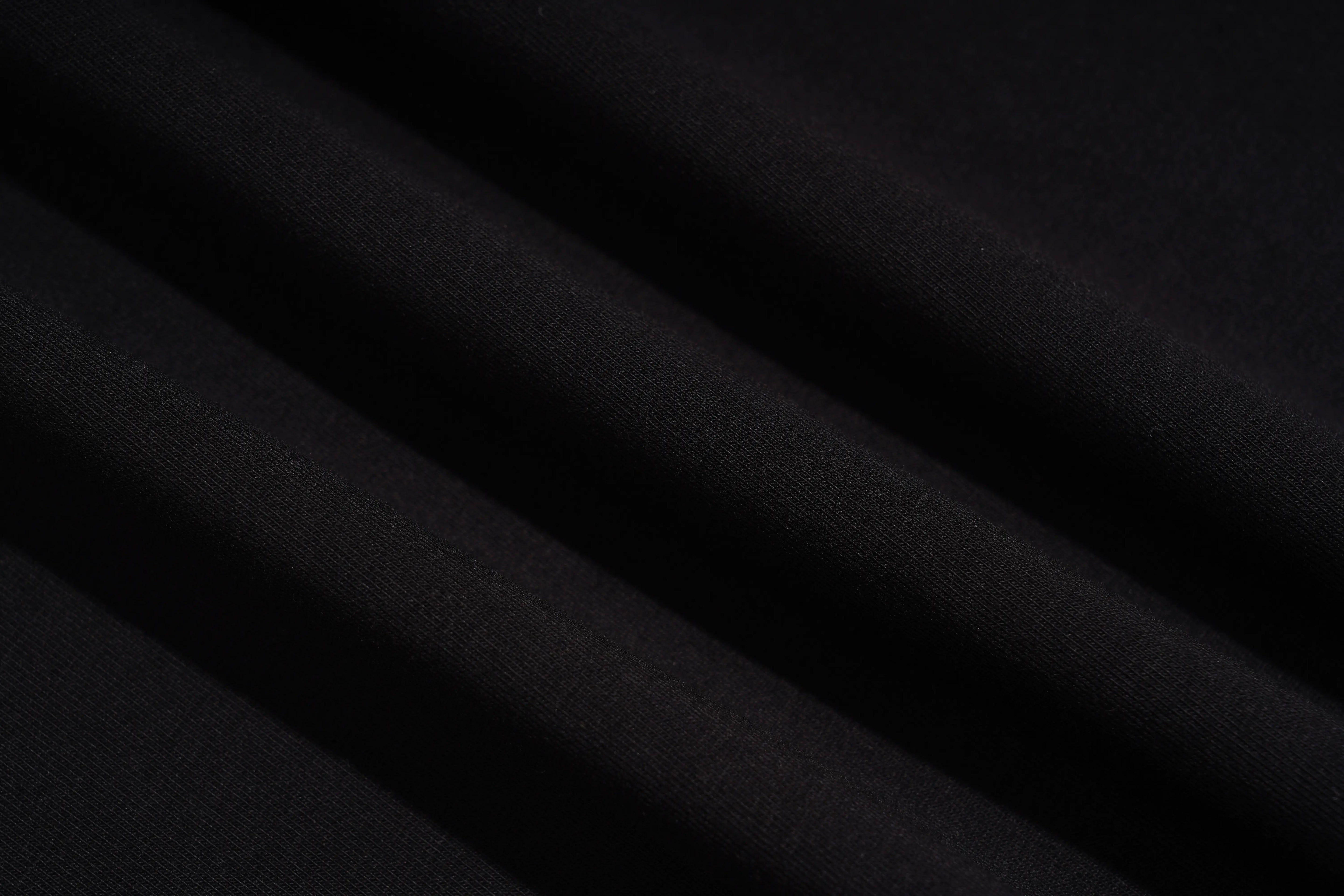 A close-up of draped black fabric with soft diagonal folds showing a fine woven texture. TCH Rhinestone Galaxy Spiral Graphic Black T-Shirt