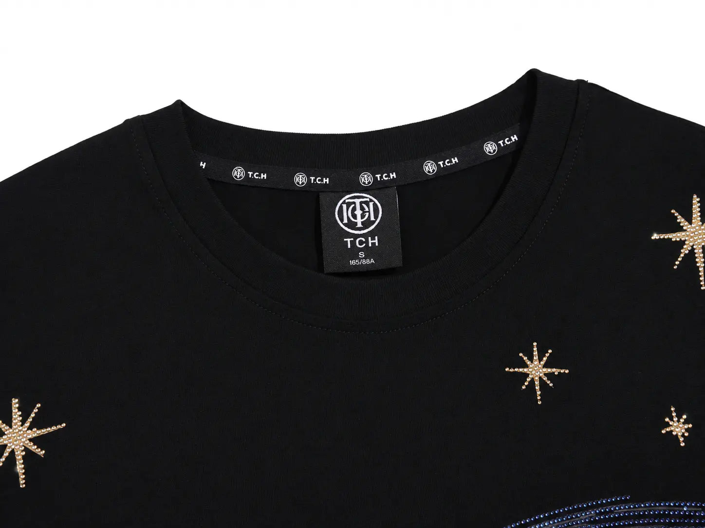 Close-up of a black crewneck sweatshirt featuring gold glitter starburst embellishments on the front, with a visible TCH brand label inside the collar. TCH Rhinestone Galaxy Spiral Graphic Black T-Shirt