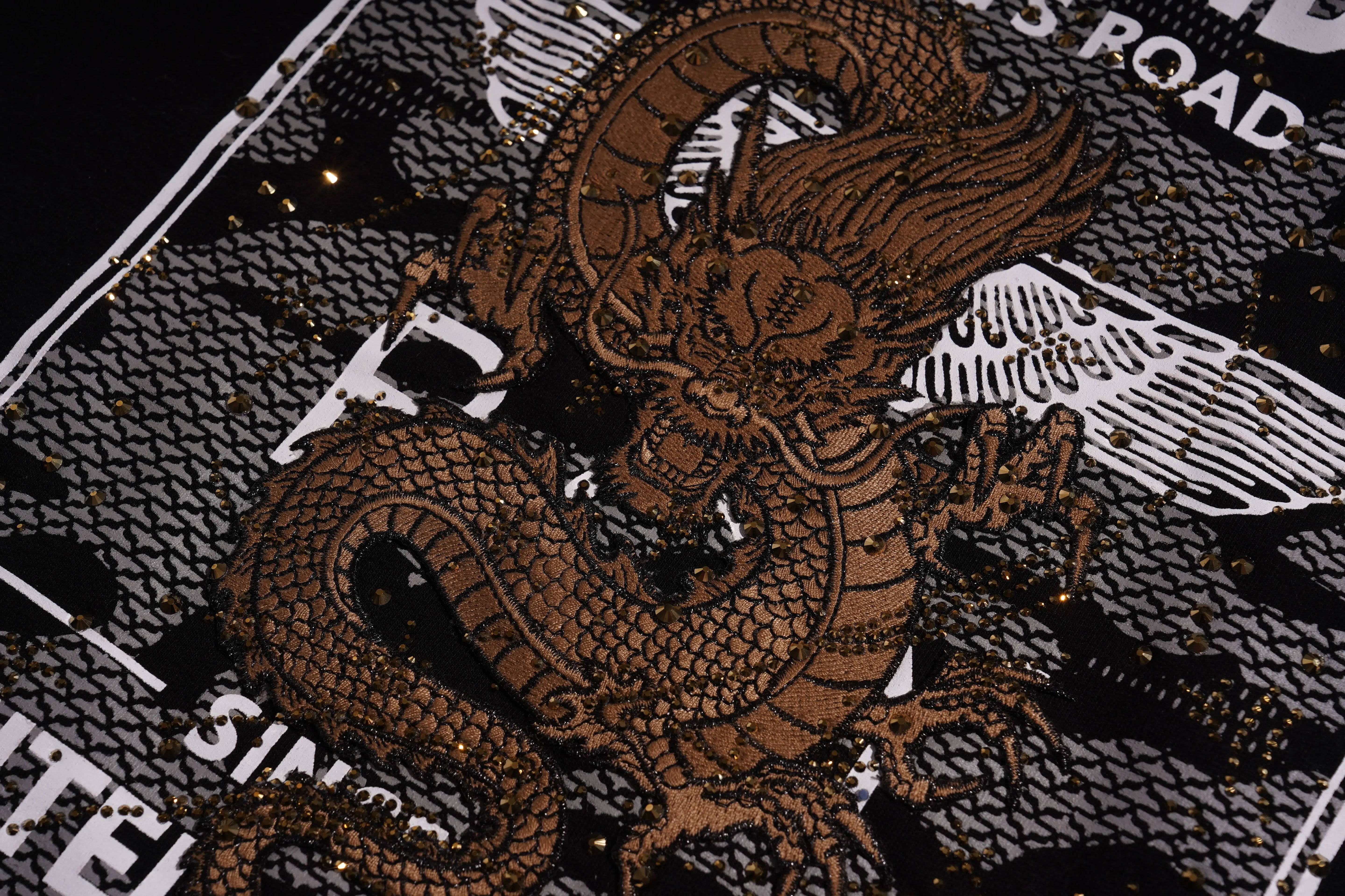 Close-up of a brown dragon design on a textured surface with text in the background. TCH Rhinestone Gold Dragon Poster Sweatshirt