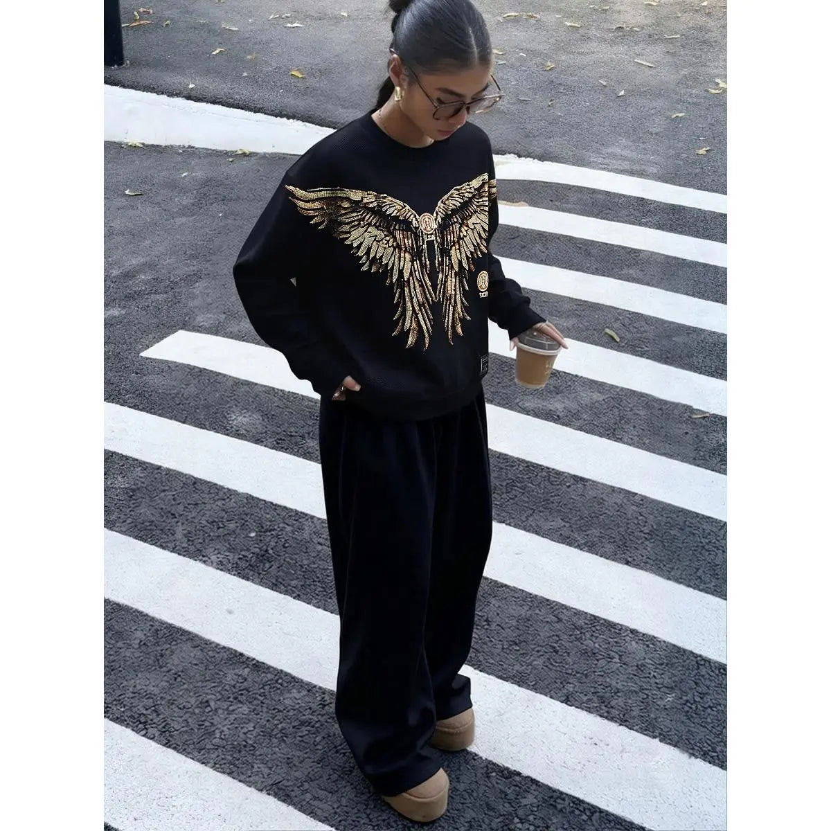 Person wearing a black outfit with a gold eagle design on a crosswalk, TCH Rhinestone Golden Wings Sweatshirt