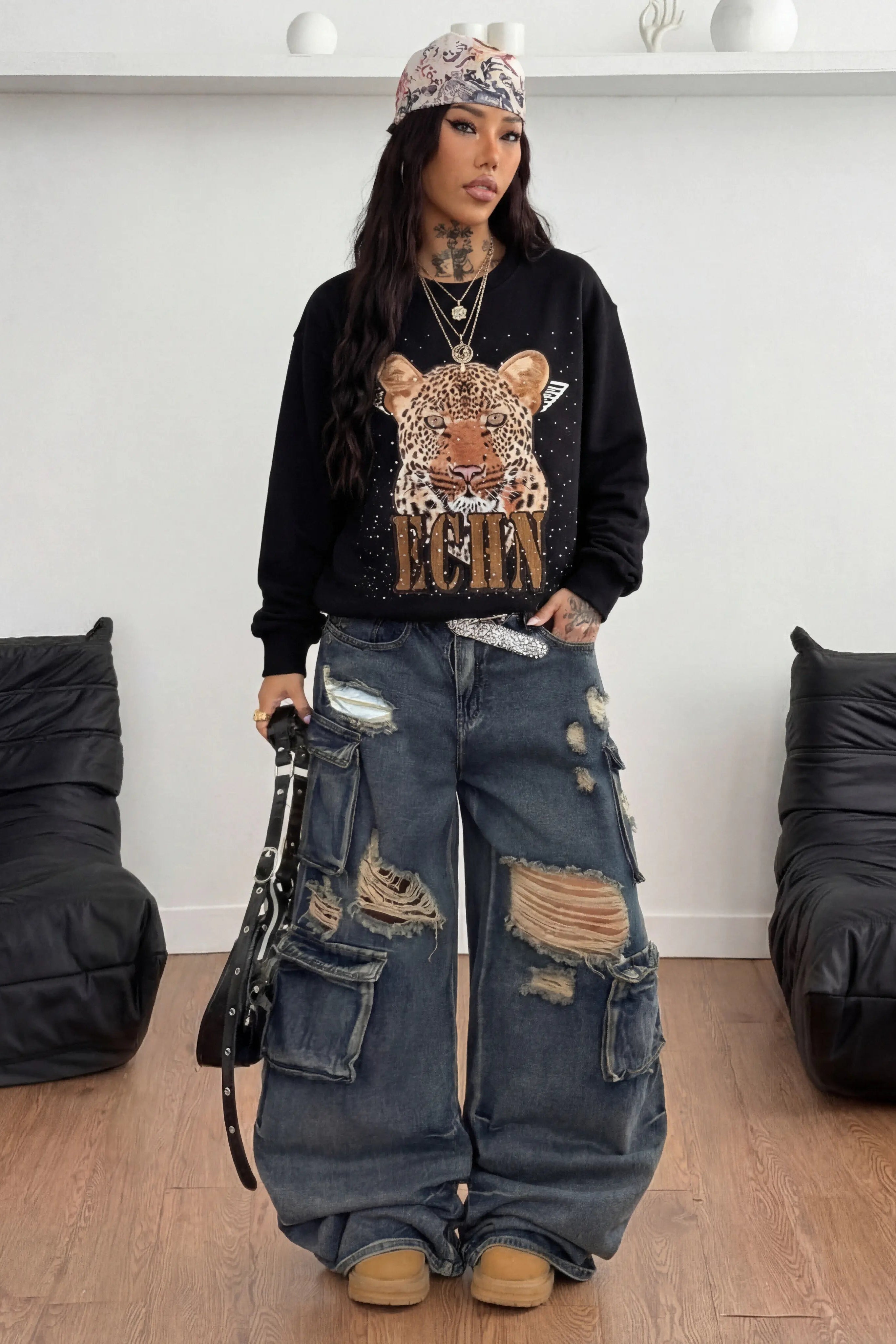 Person wearing a black sweatshirt with a graphic design and ripped jeans in a room with black bean bags. TCH Rhinestone Gradient Star Leopard Sweatshirt