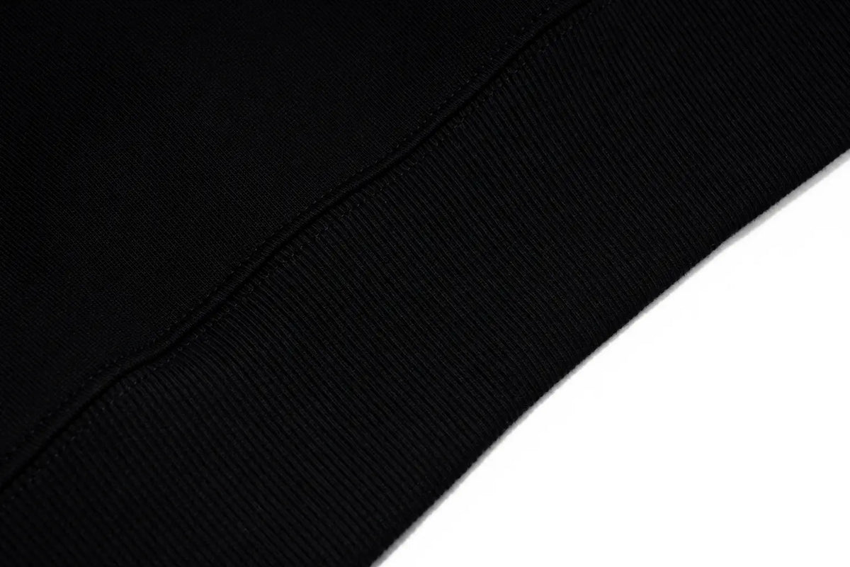Close-up of a black ribbed knit fabric, likely a sweatshirt cuff, with a clean white background visible in the lower right corner. TCH Rhinestone Graphic Black Crewneck Sweatshirt