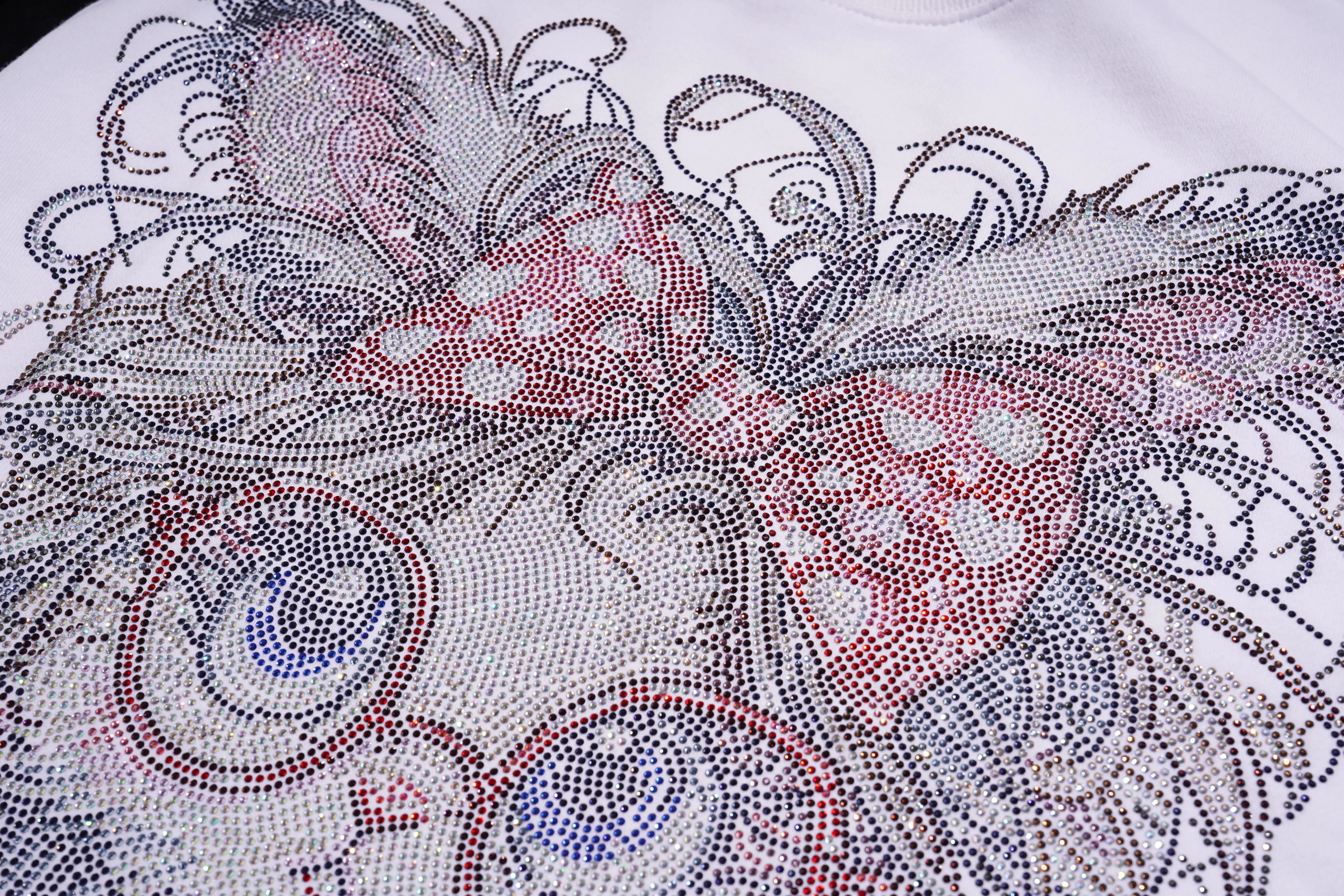 Close-up of a decorative fabric with intricate patterns and rhinestones. TCH Rhinestone Hello Kitty BOYLONDON Sweatshirt