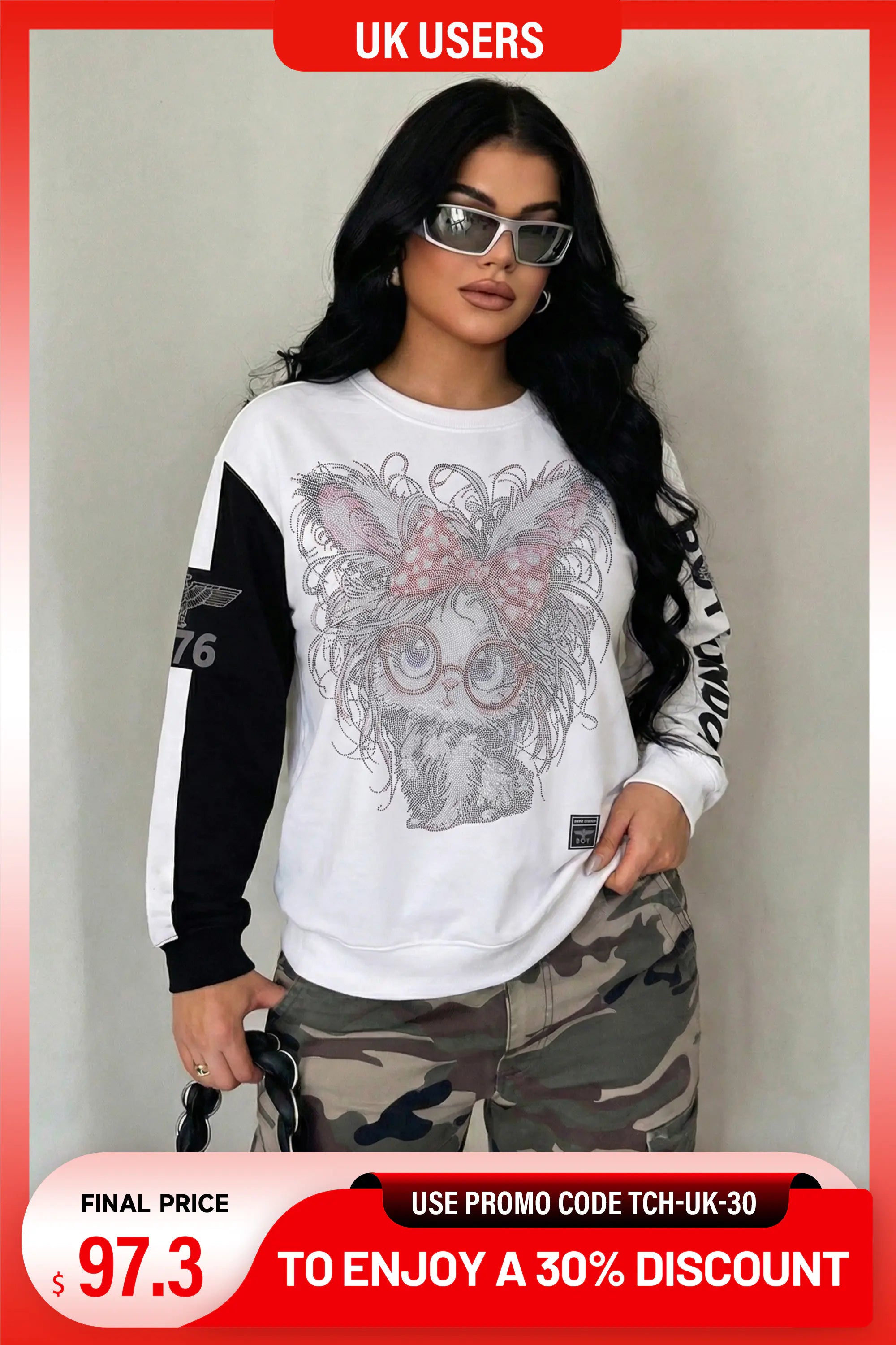 A woman modeling a white long-sleeve sweatshirt with black sleeves, featuring a large graphic of a skull wearing glasses and a pink bow on the front. She is also wearing camouflage pants and sunglasses, set against a plain light gray wall. TCH Rhinestone Hello Kitty BOYLONDON Sweatshirt 