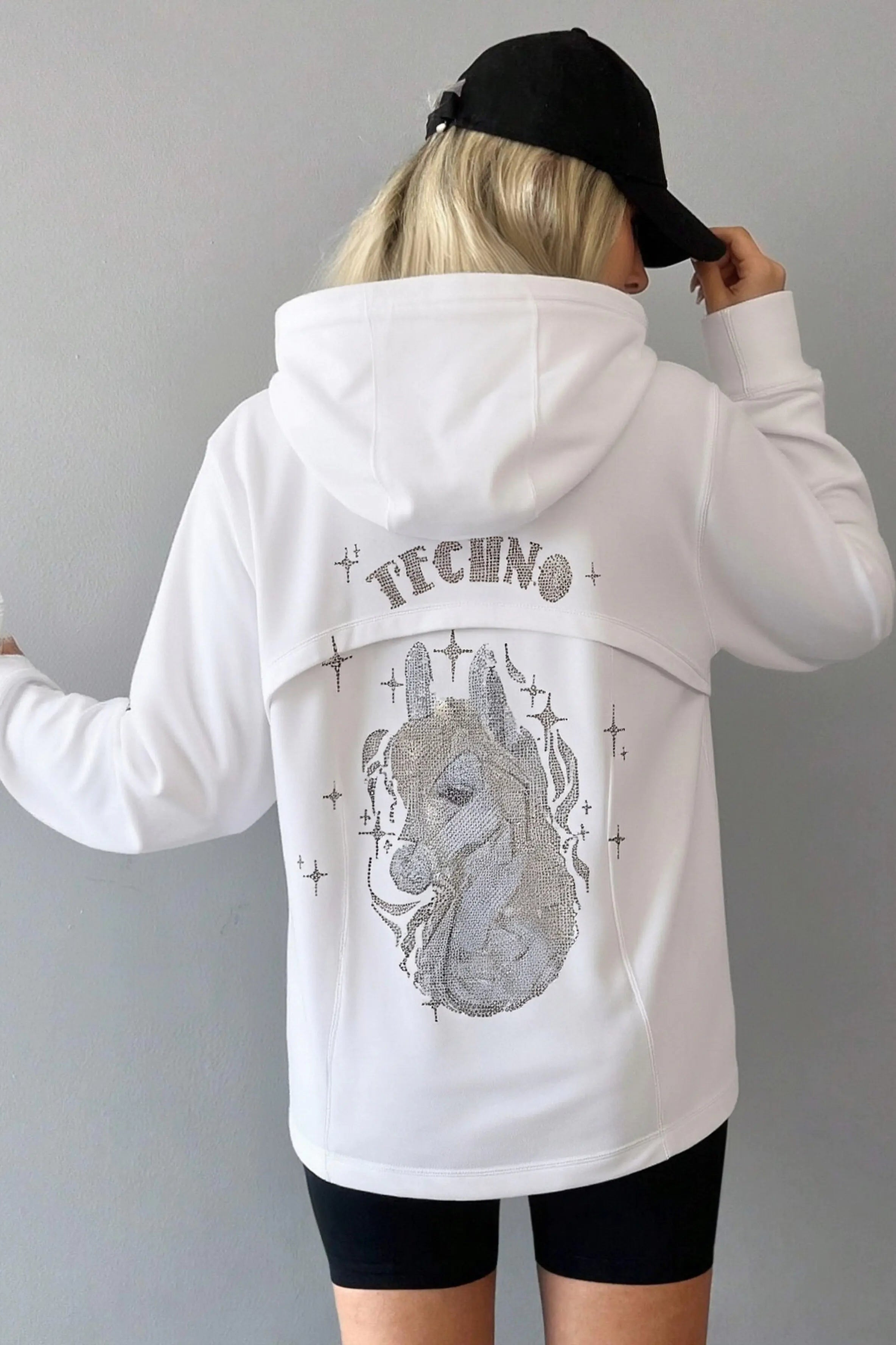 Person wearing a white hoodie with a graphic design on the back, holding a drink. TCH Rhinestone Lion & Horse Head Hoodie