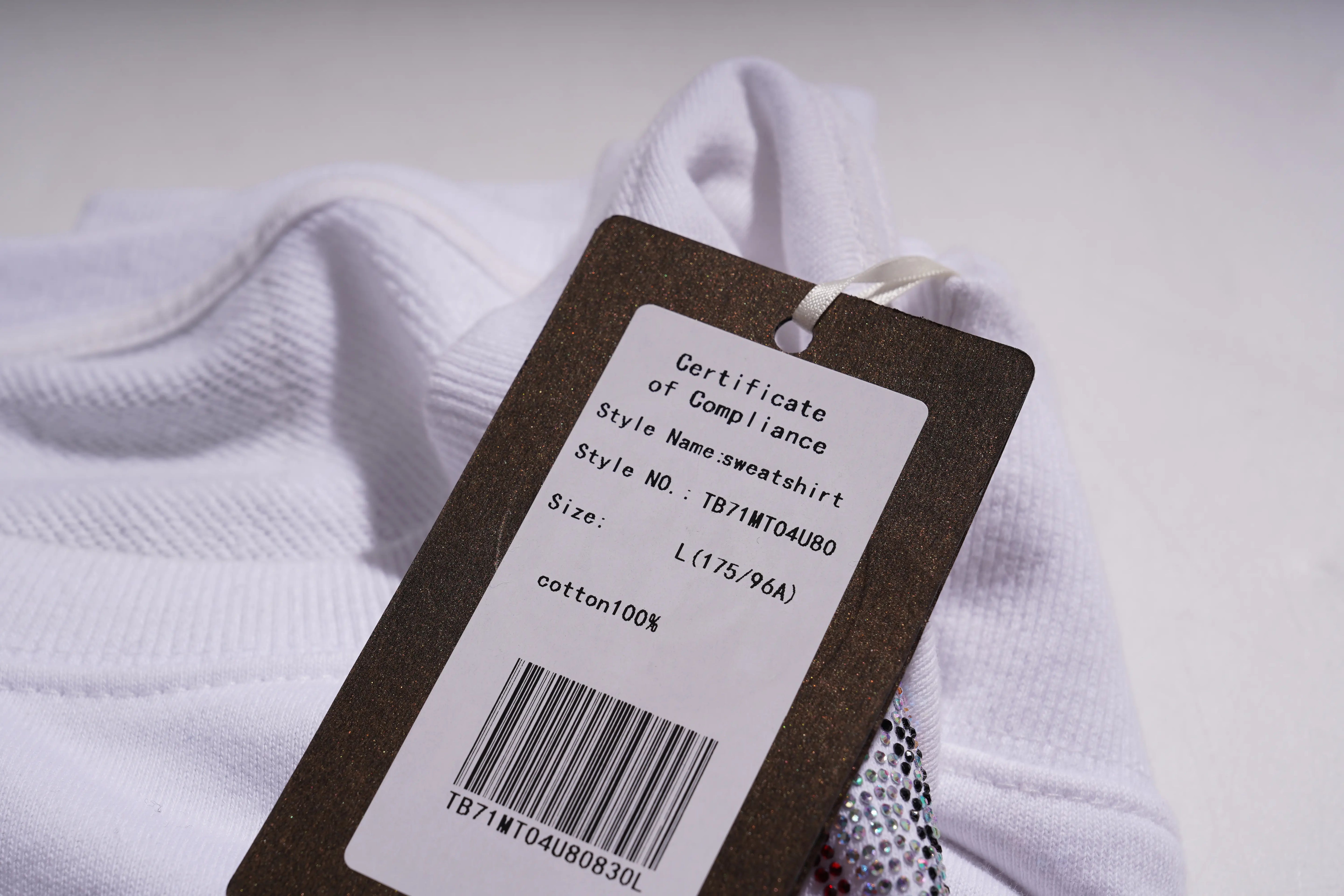 White sweatshirt with a brown tag displaying text and a barcode on a light gray background