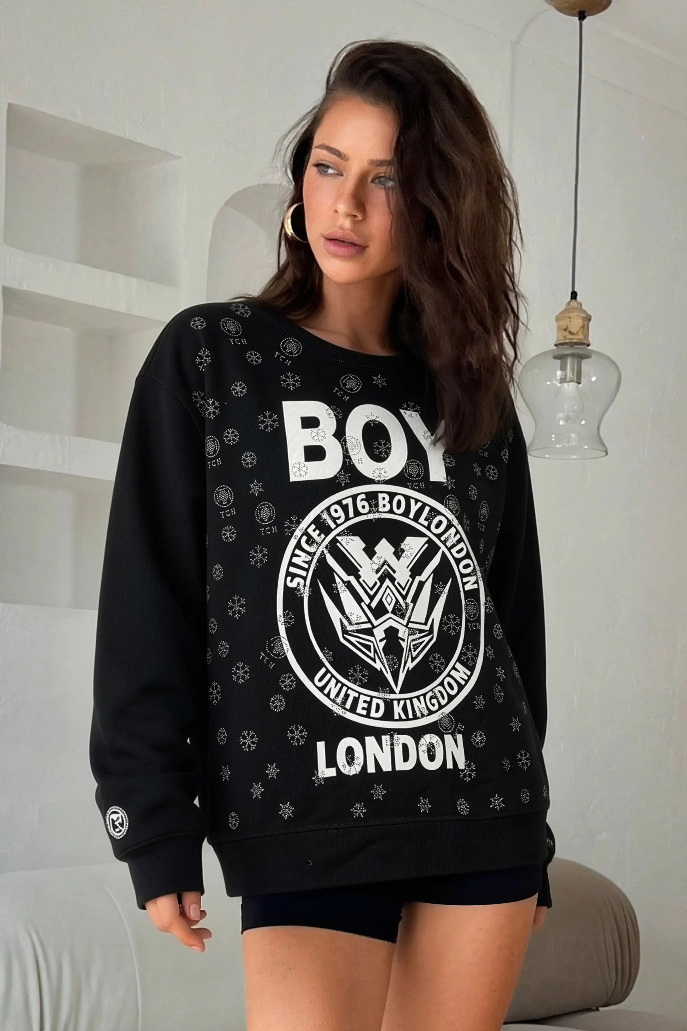 Woman wearing a black sweatshirt with 'BOY' and 'London' text in a modern indoor setting， TCH Rhinestone Mech Logo Crew Neck Sweatshirt