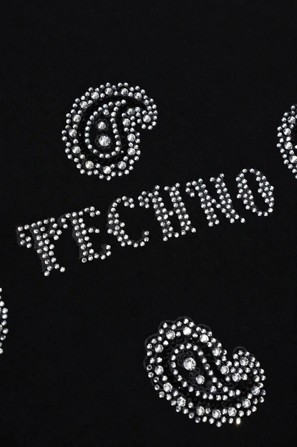 A close-up of a black garment featuring silver rhinestone lettering that spells 'TECHNO' and matching paisley embellishments. TCH Rhinestone Paisley Pattern Long Sleeve Polo Shirt
