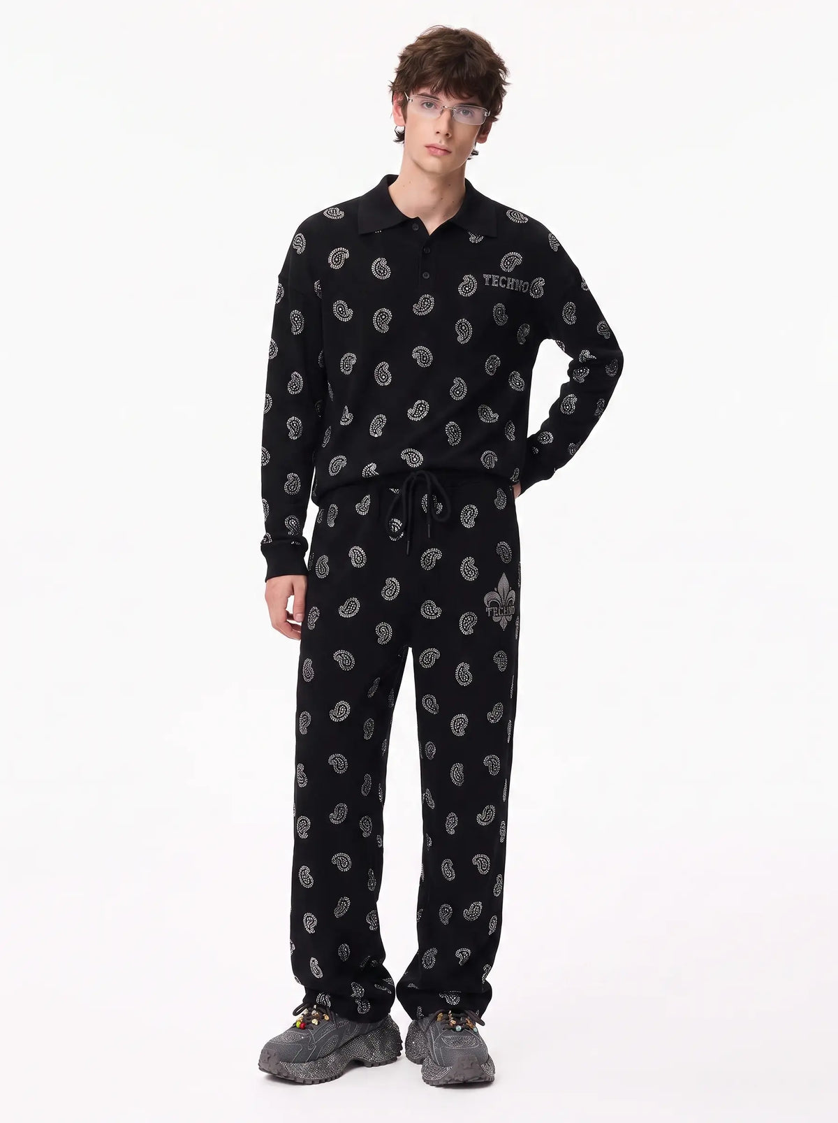 A man modeling a black long-sleeve polo shirt and matching sweatpants set, both covered in a small gray paisley pattern. The shirt features a gray 'TACTICAL' logo on the left chest. TCH Rhinestone Paisley Pattern Long Sleeve Polo Shirt