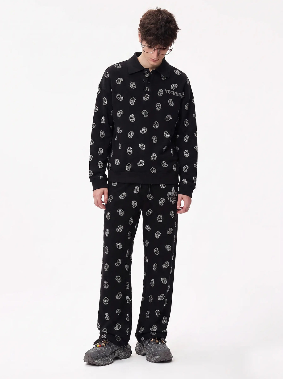 A model wearing a black two-piece tracksuit with a white circular pattern, featuring a long-sleeve collared shirt and matching pants, paired with gray sneakers against a plain white background. TCH Rhinestone Paisley Pattern Long Sleeve Polo Shirt