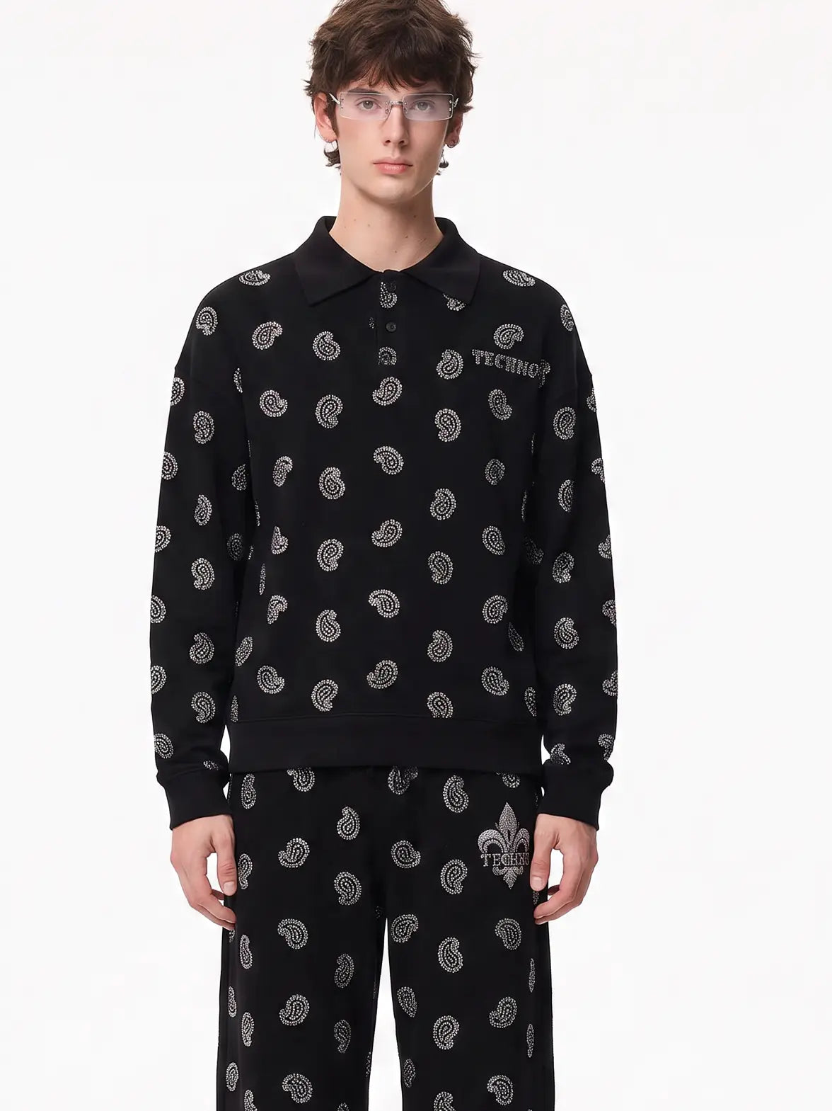 A model wearing a black long-sleeve polo sweatshirt and matching pants with a repeating white paisley pattern, featuring the TECHIO brand name on the chest. TCH Rhinestone Paisley Pattern Long Sleeve Polo Shirt
