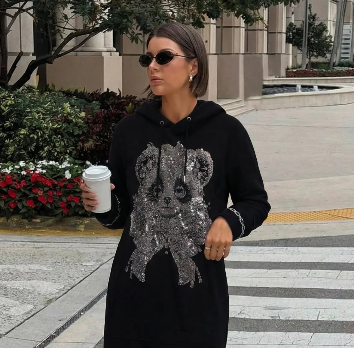 Woman wearing a black hoodie with a sequined bear design, holding a coffee cup outdoors. TCH Rhinestone Panda Bow Dress