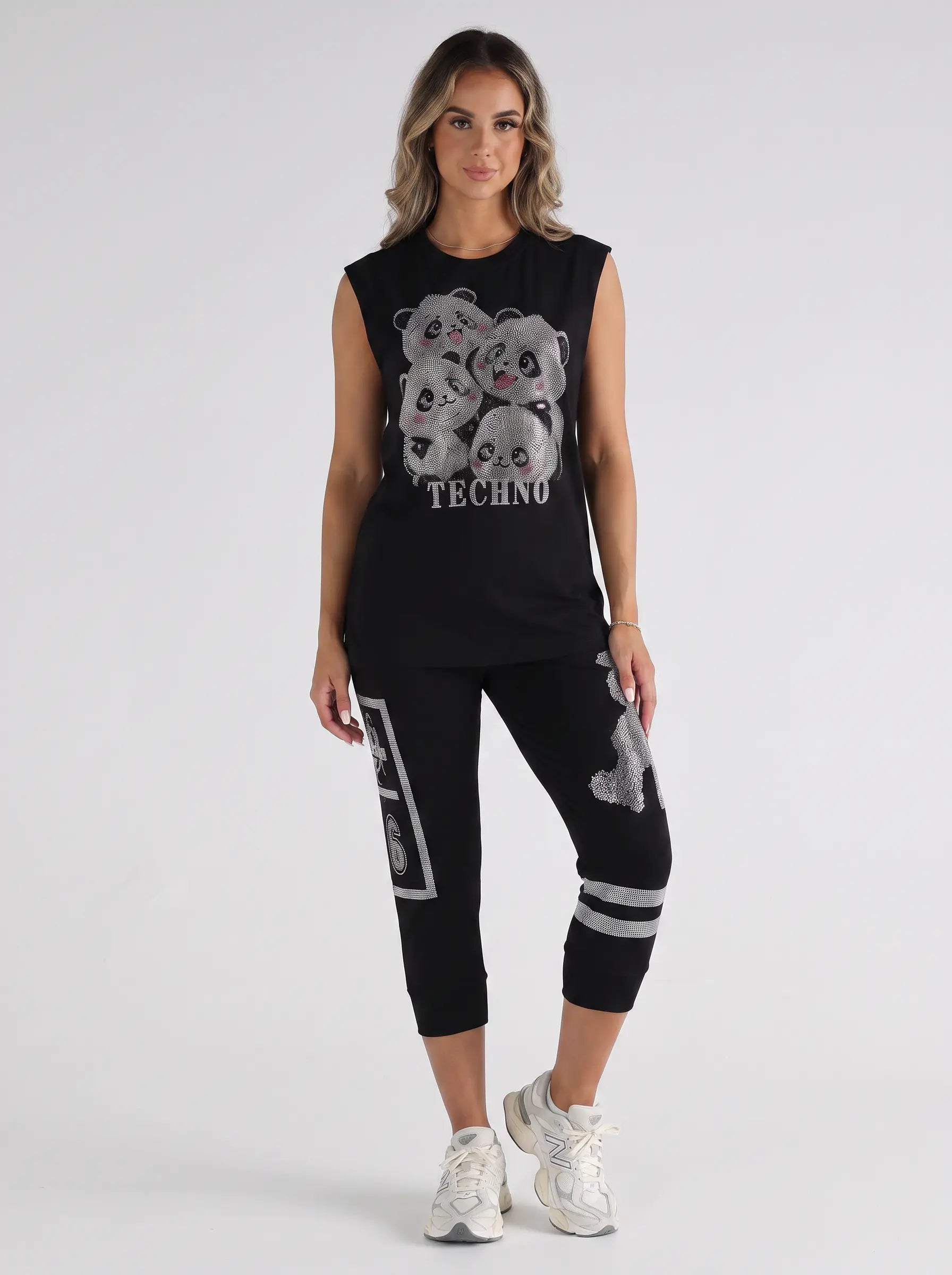 A woman modeling a black sleeveless crop top and matching black capri leggings set. The top features a large graphic of four cartoon bears with the word 'TECHNO' underneath. TCH Rhinestone Panda Graphic Sleeveless T-Shirt
