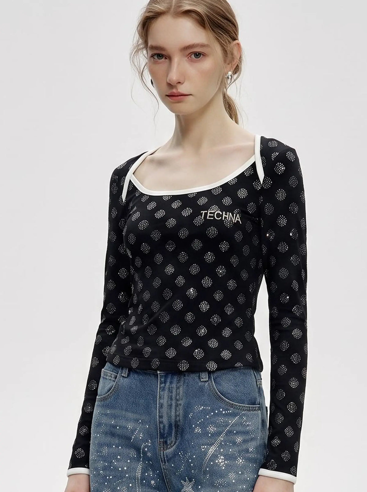 A model wearing a light blue denim jacket with various embroidered patches, including a teddy bear on the left chest and cherries on the sleeve, styled over a white t-shirt and dark pants. TCH Rhinestone Pattern Long Sleeve Top