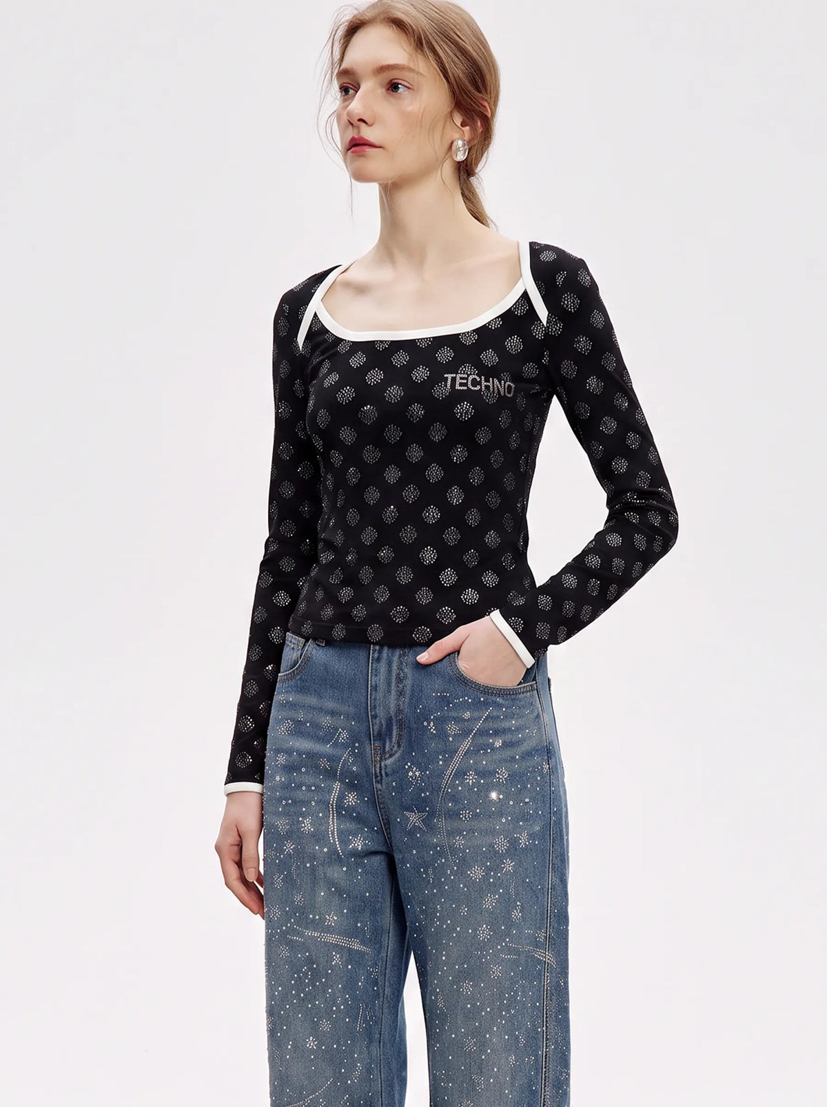 A model wearing a black long-sleeve scoop-neck top with a white trim and a small white 'TECHNO' logo on the chest, paired with blue jeans, against a plain white studio background. TCH Rhinestone Pattern Long Sleeve Top