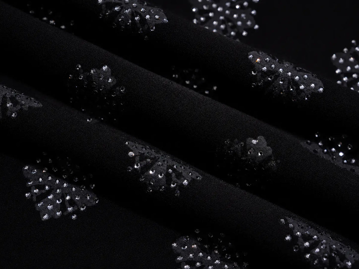 Black fabric with repeating clusters of small silver rhinestones arranged in a floral or starburst pattern, shown in a close-up draped view. TCH Rhinestone Pattern Long Sleeve Top