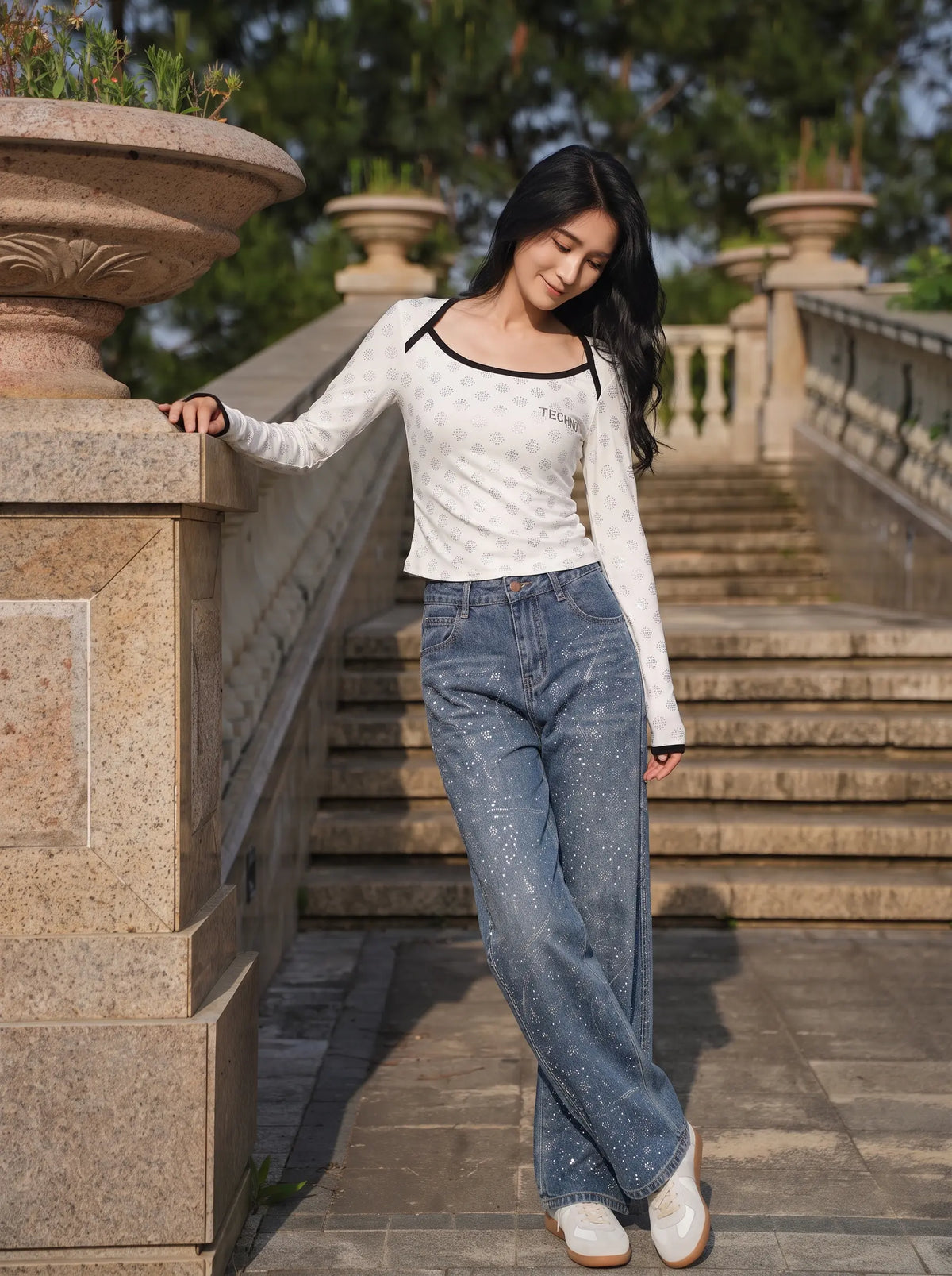 A woman posing on outdoor stone stairs wearing a white long-sleeve knit top with black trim and blue jeans. TCH Rhinestone Pattern Long Sleeve Top