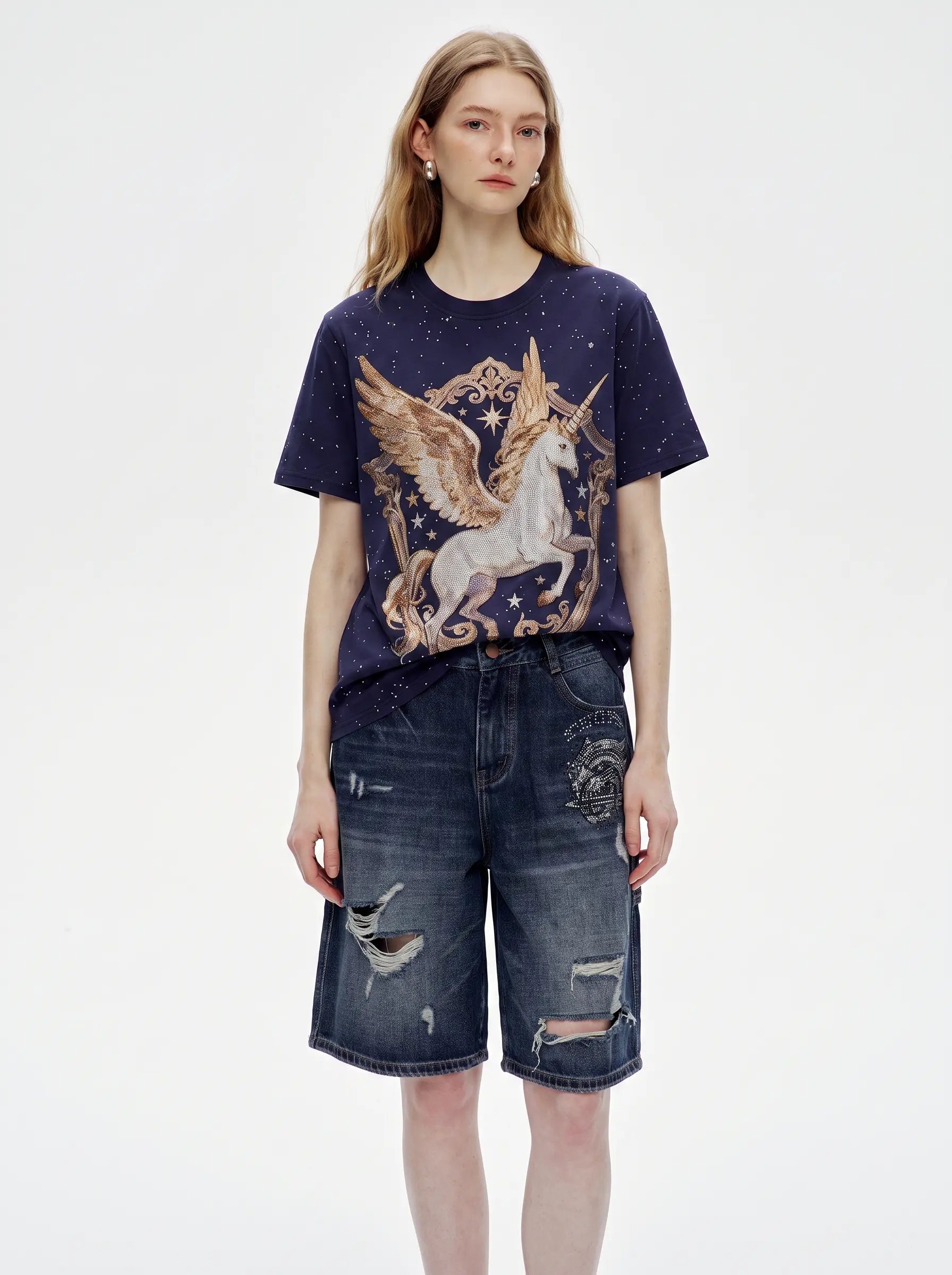 A model wearing a navy blue t-shirt with a large gold and white winged unicorn graphic, paired with distressed dark blue denim shorts, against a plain white studio background. TCH Rhinestone Pegasus Wing Graphic Navy Blue T-Shirt