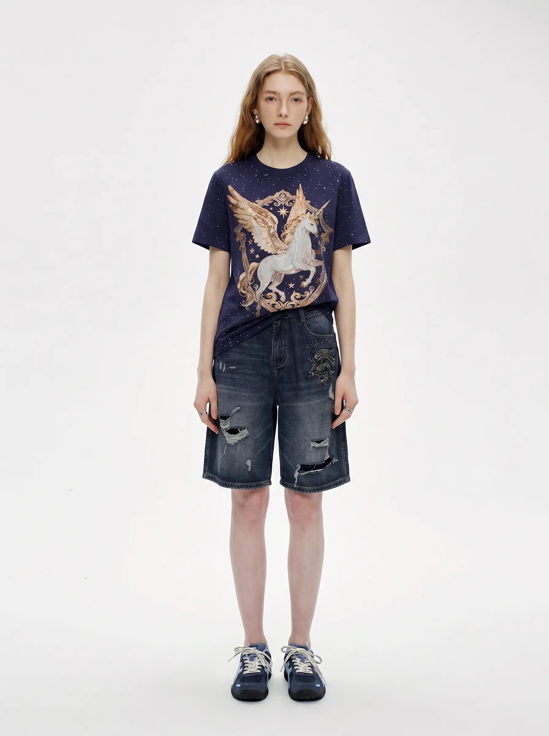 A model stands against a plain light gray studio background wearing a navy graphic T-shirt with a large winged horse print, distressed denim shorts, and dark sneakers. TCH Rhinestone Pegasus Wing Graphic Navy Blue T-Shirt