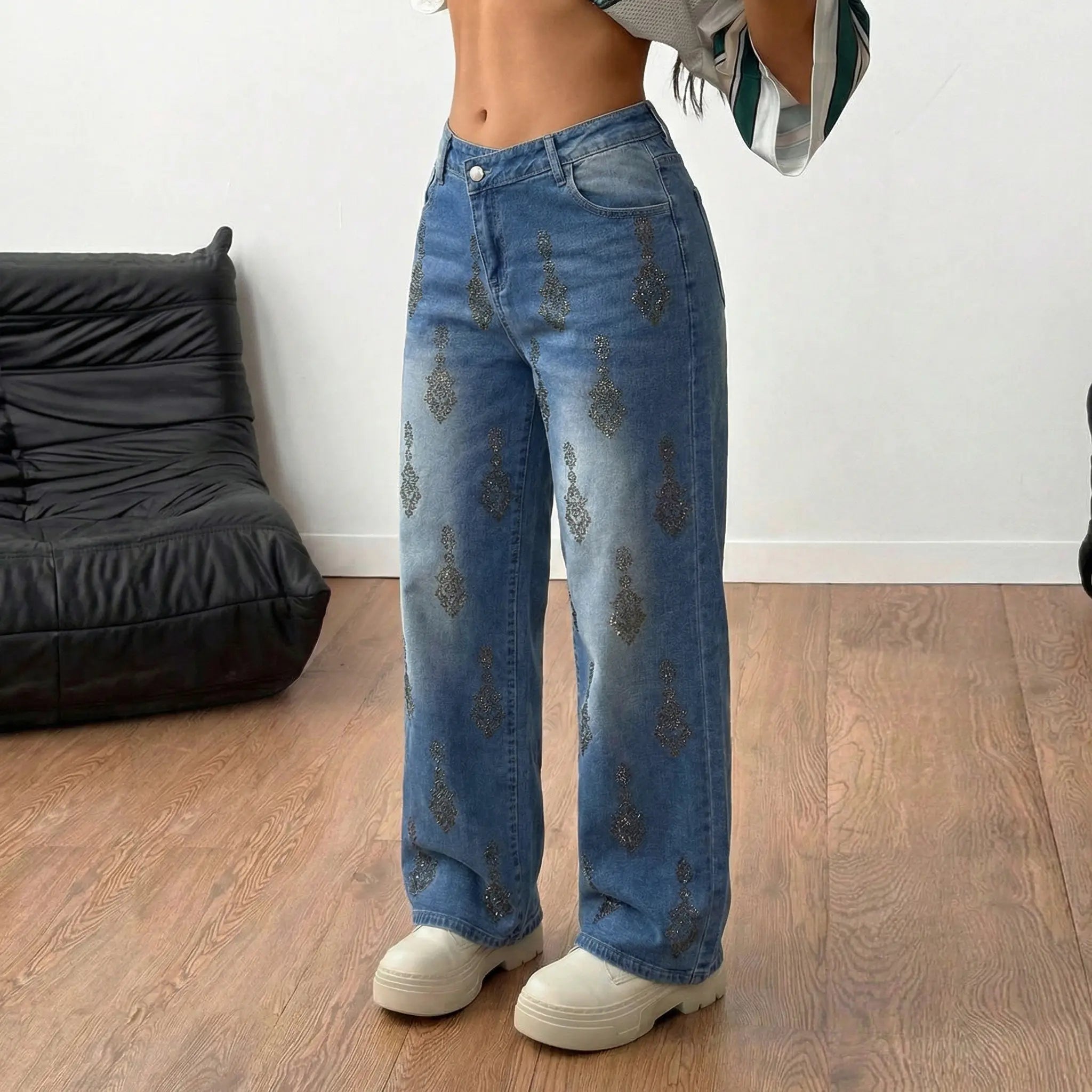 Person wearing blue jeans and white shoes standing on a wooden floor with a black bean bag chair in the background. TCH Rhinestone Pendant Allover Denim Jeans