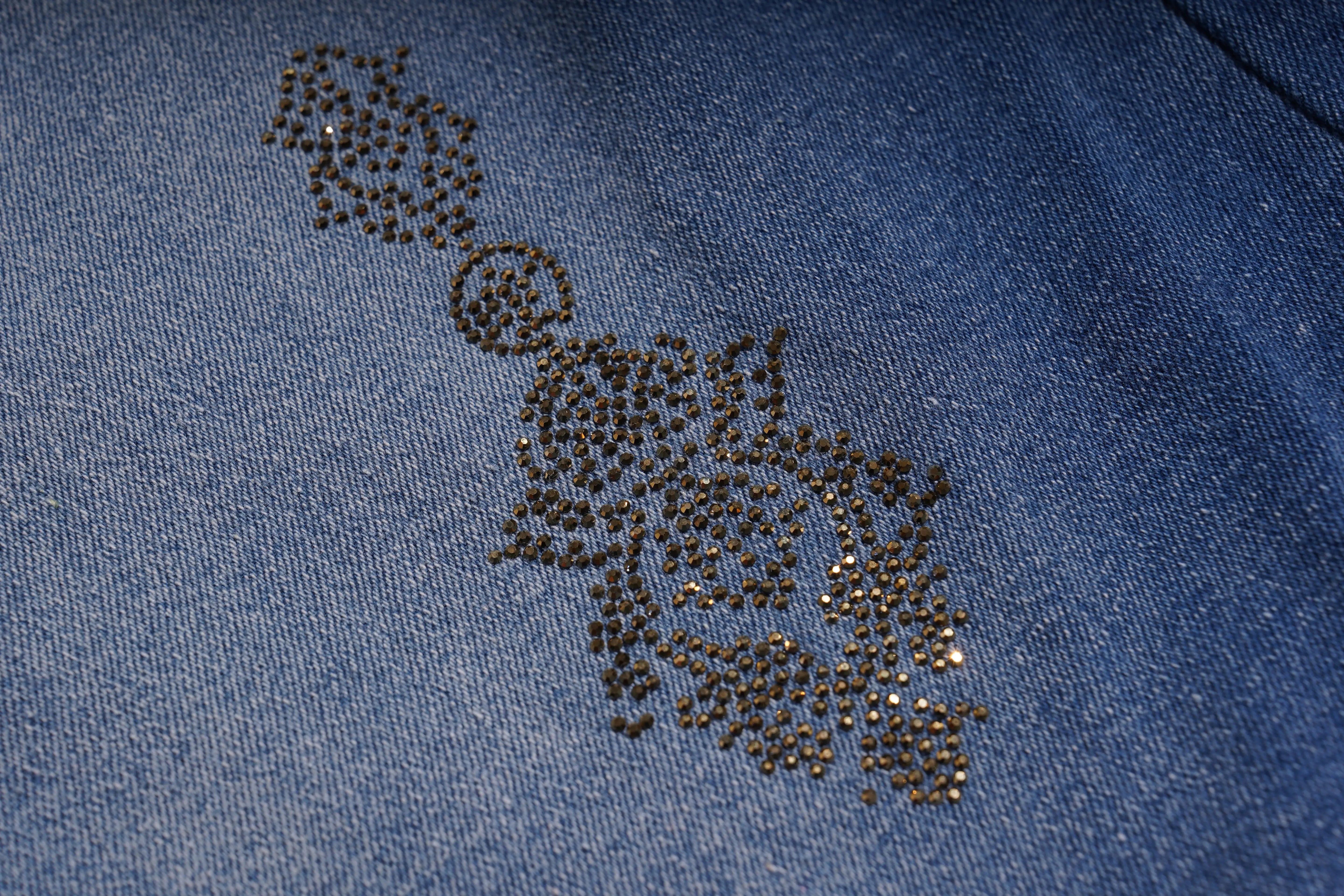 Close-up of a blue fabric with decorative black rhinestone pattern, TCH Rhinestone Pendant Allover Denim Jeans