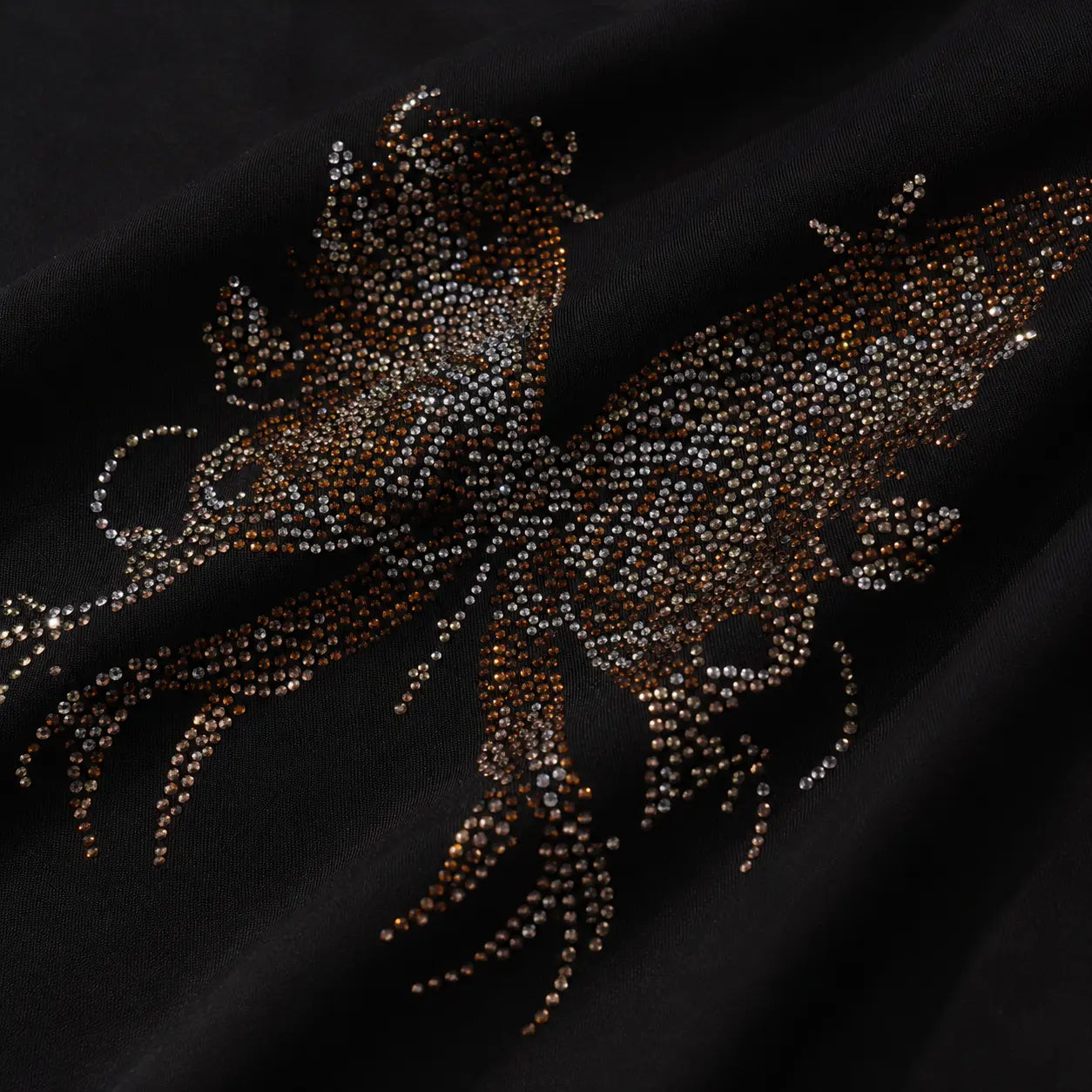 A close-up of a black fabric featuring an intricate, glittering butterfly embellishment made of shimmering brown and silver rhinestones. TCH Rhinestone Phoenix Cargo Wide-Leg Pants