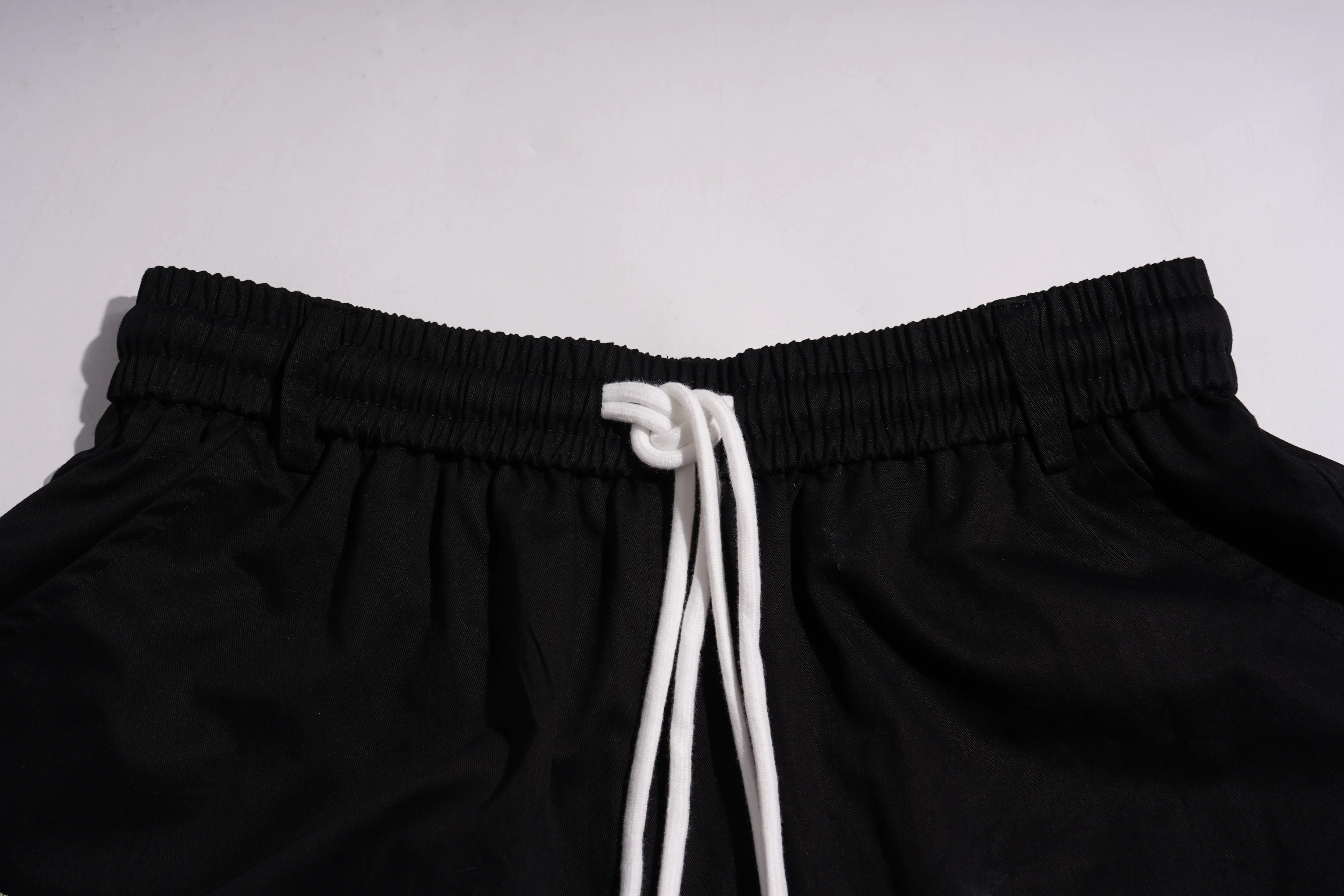 Close-up of black shorts with a white drawstring at the elastic waistband, photographed against a plain light background.