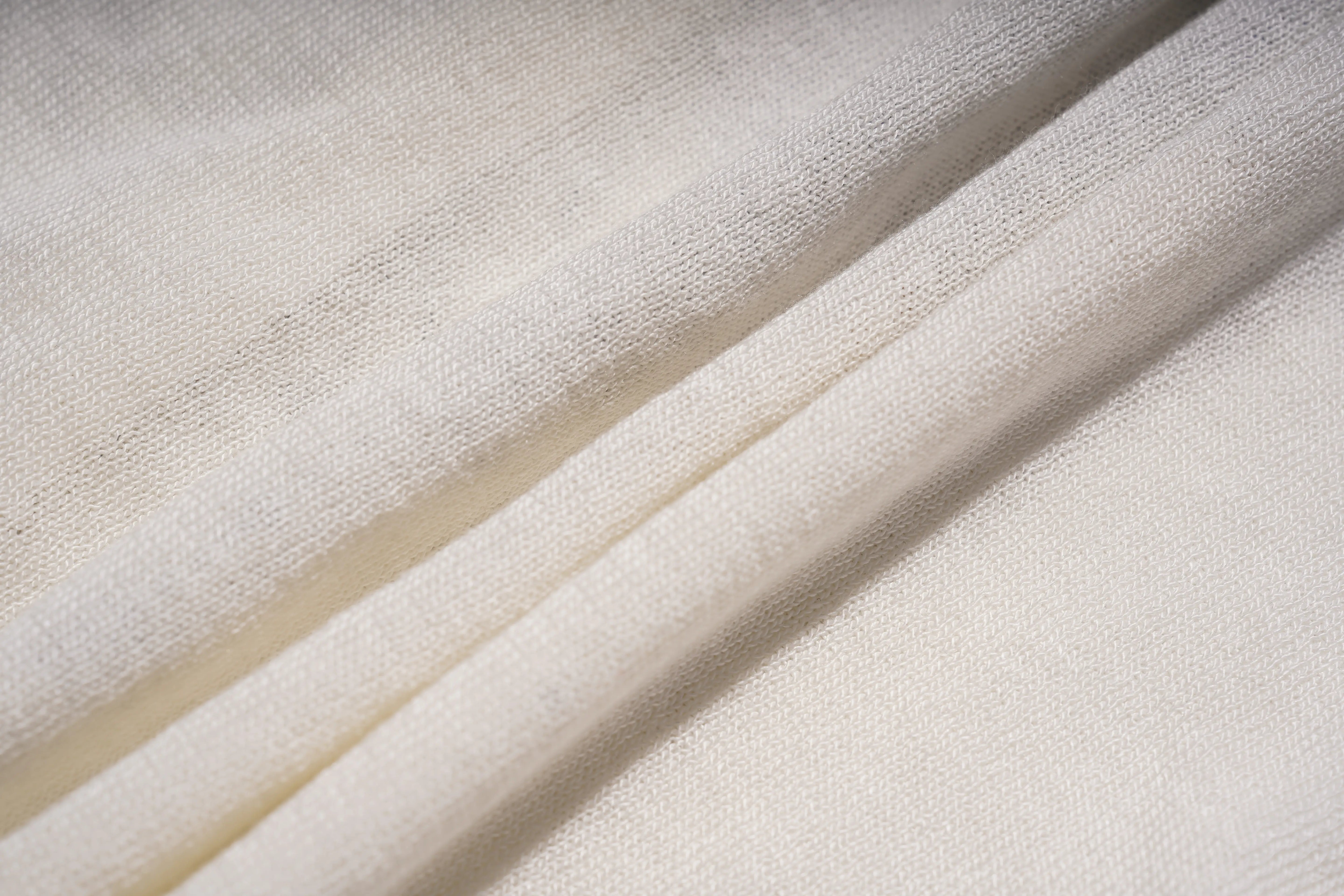 A close-up of draped off-white or cream-colored fabric with a soft, textured weave and gentle folds. TCH Rhinestone Phoenix Wings Button Knit Top
