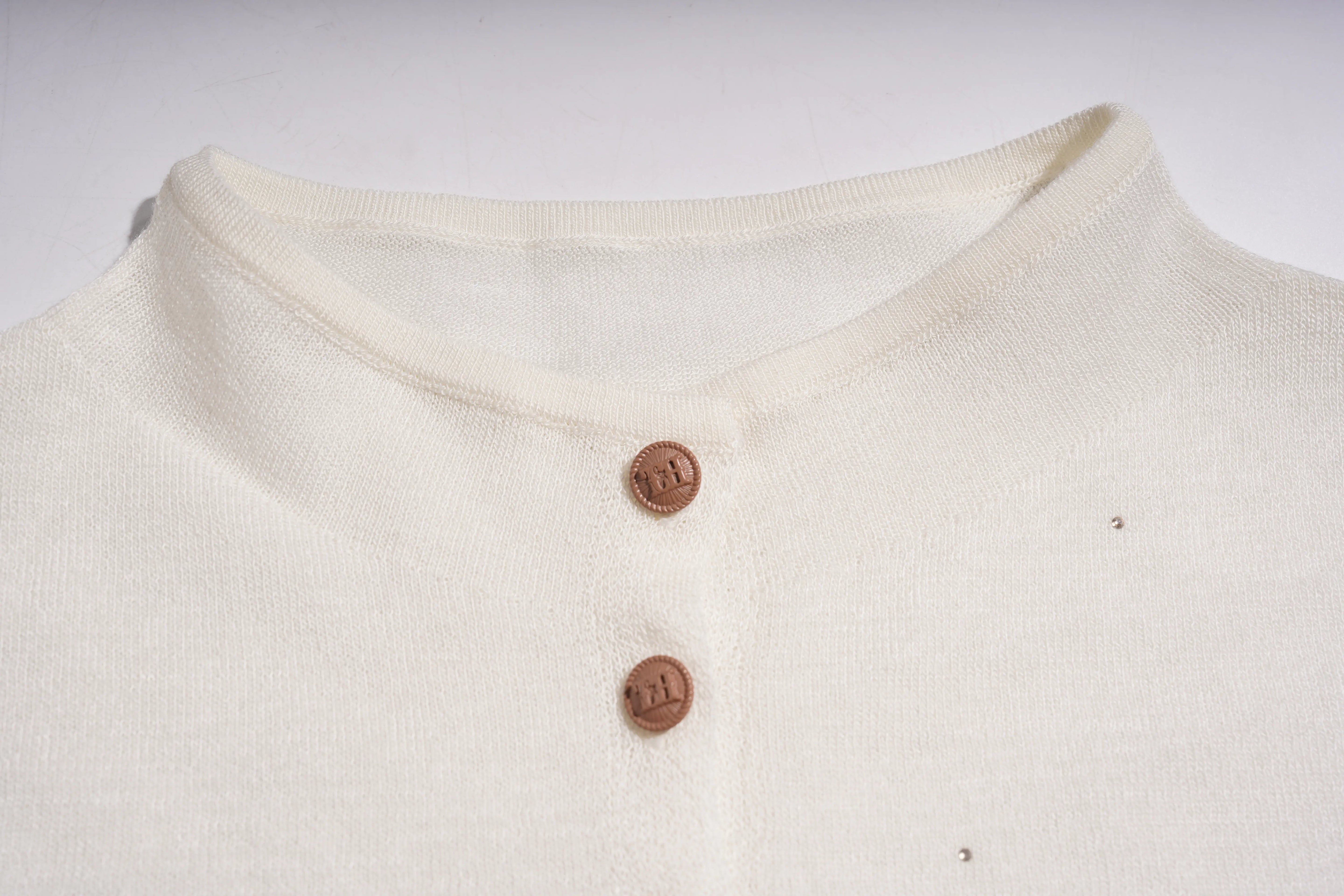 Close-up of a cream-colored knit top with a short button placket and brown buttons, laid flat against a light background. TCH Rhinestone Phoenix Wings Button Knit Top