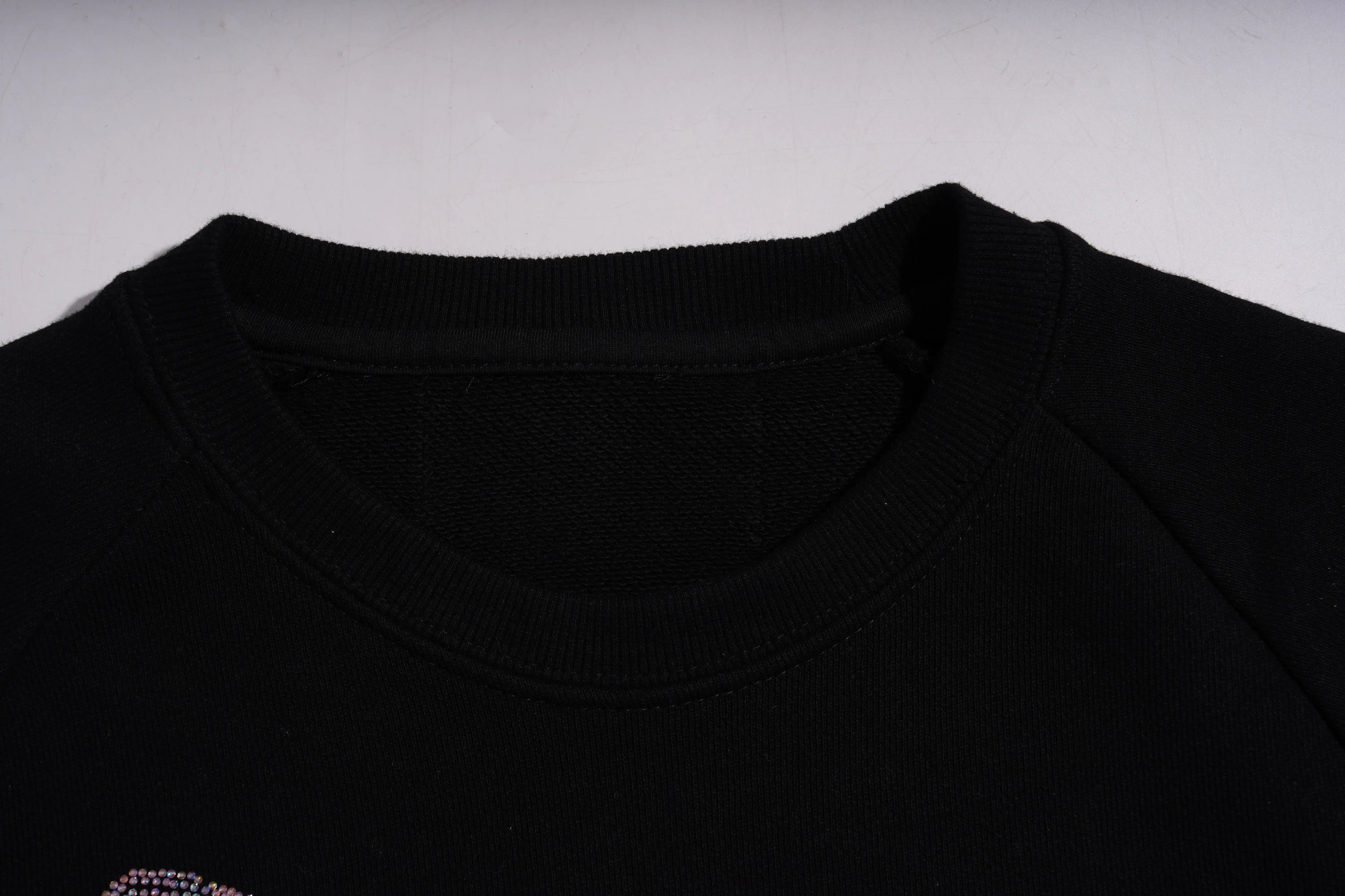 Close-up of a black garment with a brand logo on a light gray background, TCH Rhinestone Pink Bear Skull Sleeve Sweatshirt