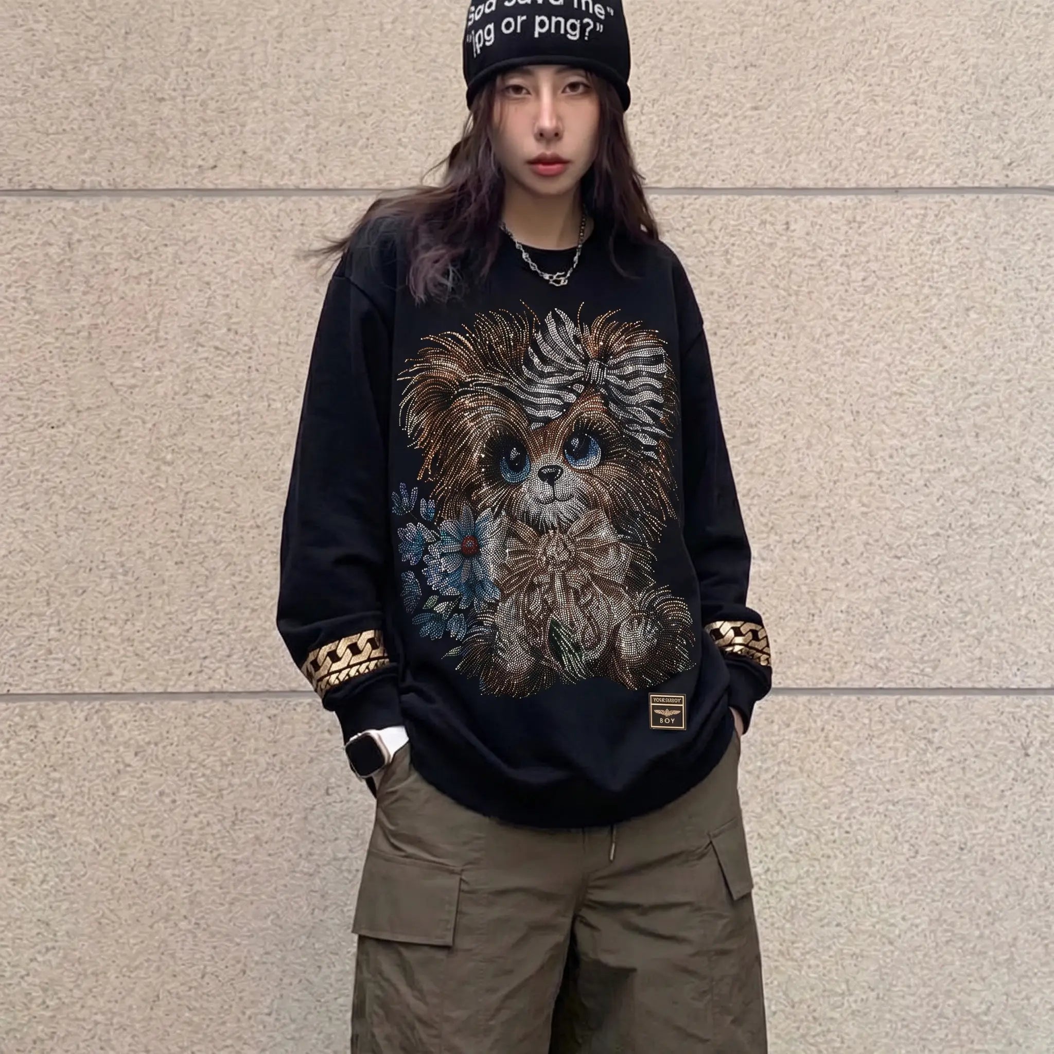 Person wearing a black sweatshirt with a graphic design of a creature, standing against a beige wall. TCH Rhinestone Puppy Black Streetwear Sweatshirt