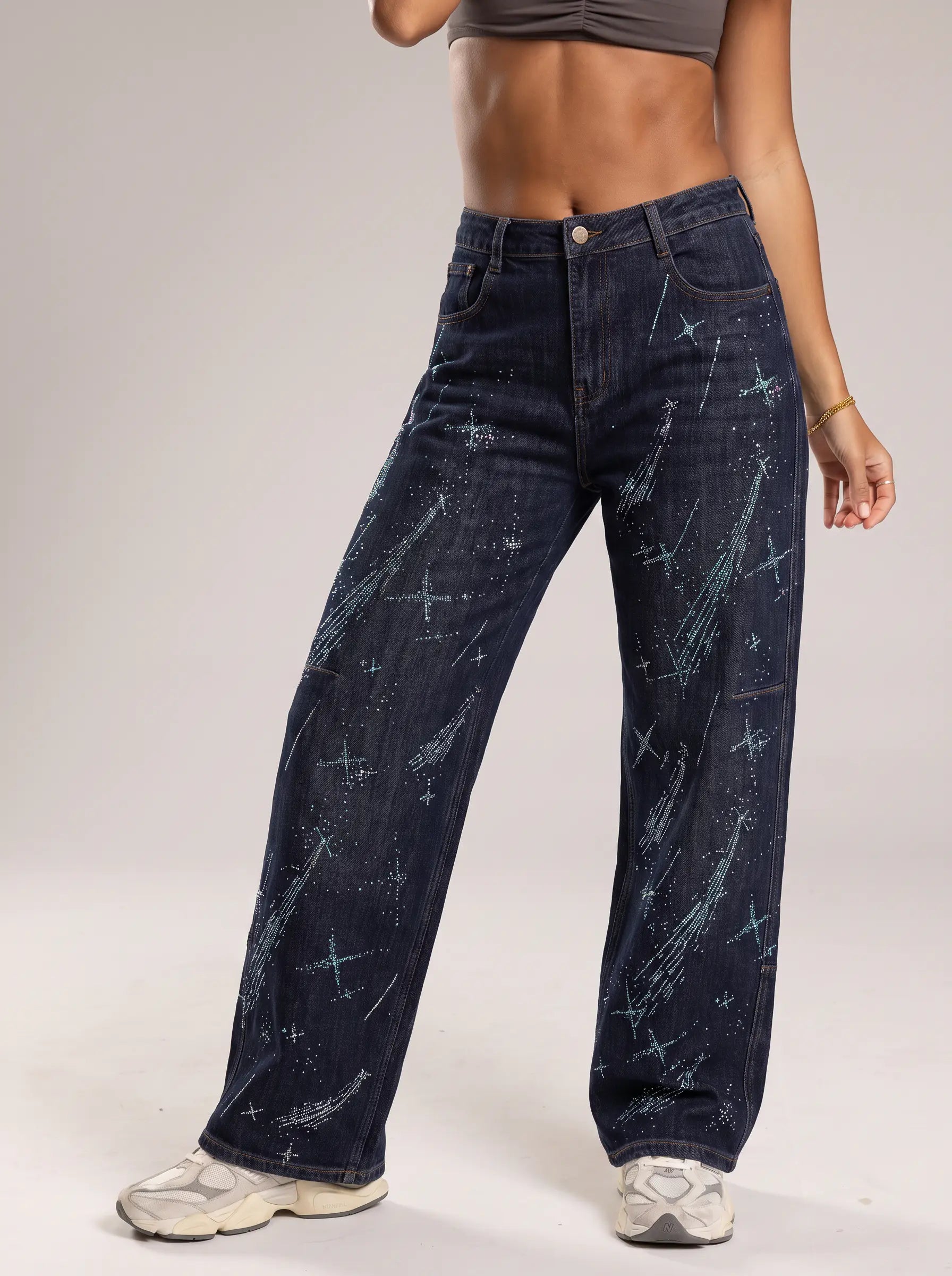 A model wearing dark blue wide-leg jeans with a light blue and white starry space print, paired with white sneakers, shown from the waist down against a neutral studio background. TCH Rhinestone Shooting Star Galaxy Jeans