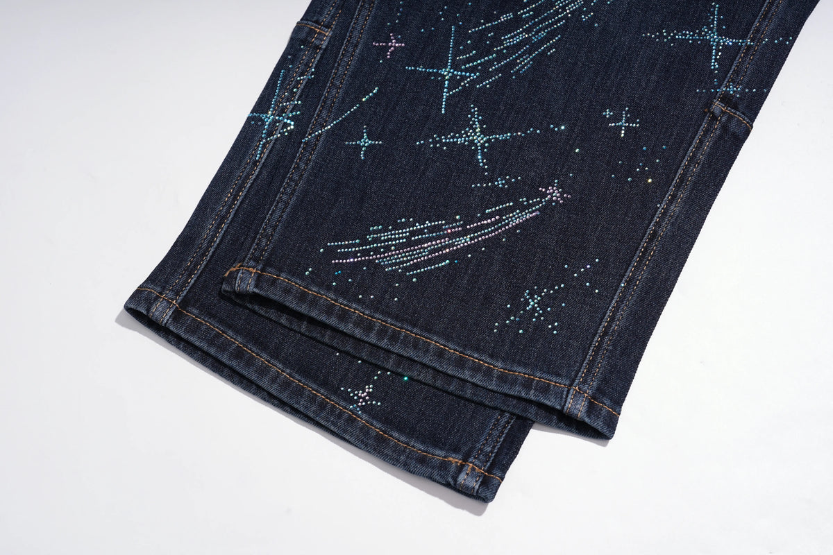 Dark blue denim jeans folded on a white background, decorated with rhinestone star and shooting star patterns. TCH Rhinestone Shooting Star Galaxy Jeans